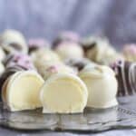 cut open white chocolate truffle on a clear glass plate with other truffles in the background
