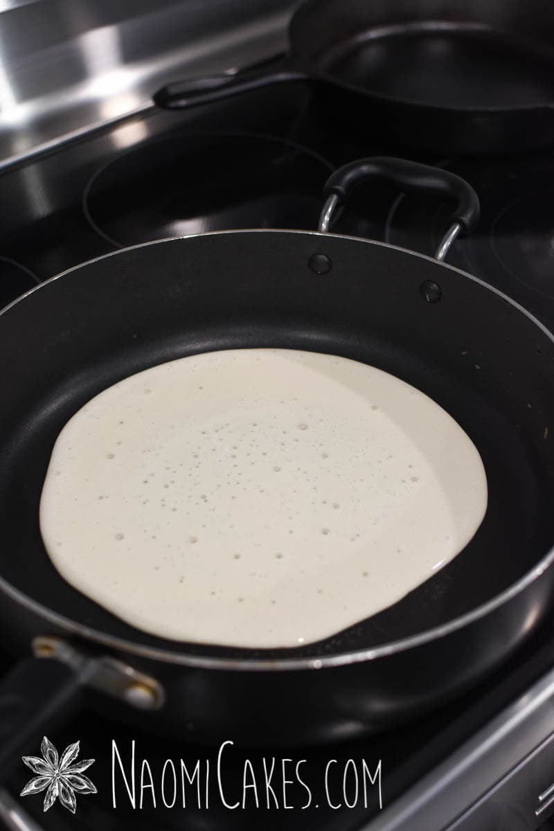 thin crepe batter in a non stick pan on an electric stovetop