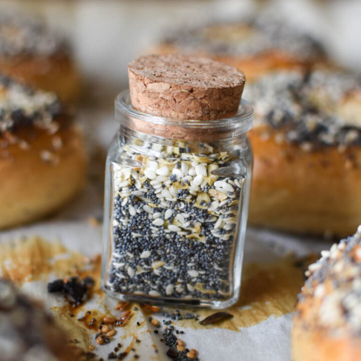 cork lid jar of everything bagel seasoning on a pan with 6 fresh baked everything bagels