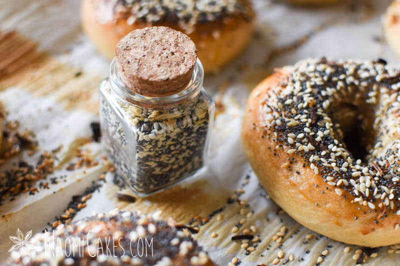close up closed cork lid jar of everything bagel seasoning on a pan with fresh baked everything bagels