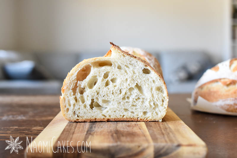 half a loaf of cut white sourdough bread to show the crumb on a wooden cutting board