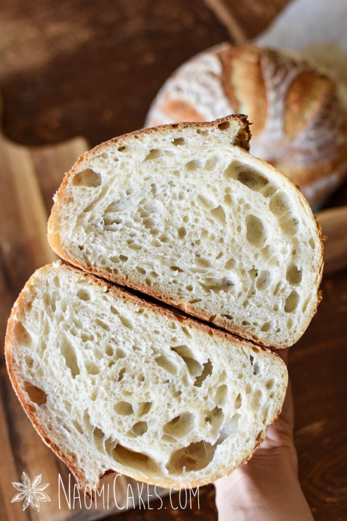 hand holding a loaf of white sourdough bread cut in half to expose the crumb