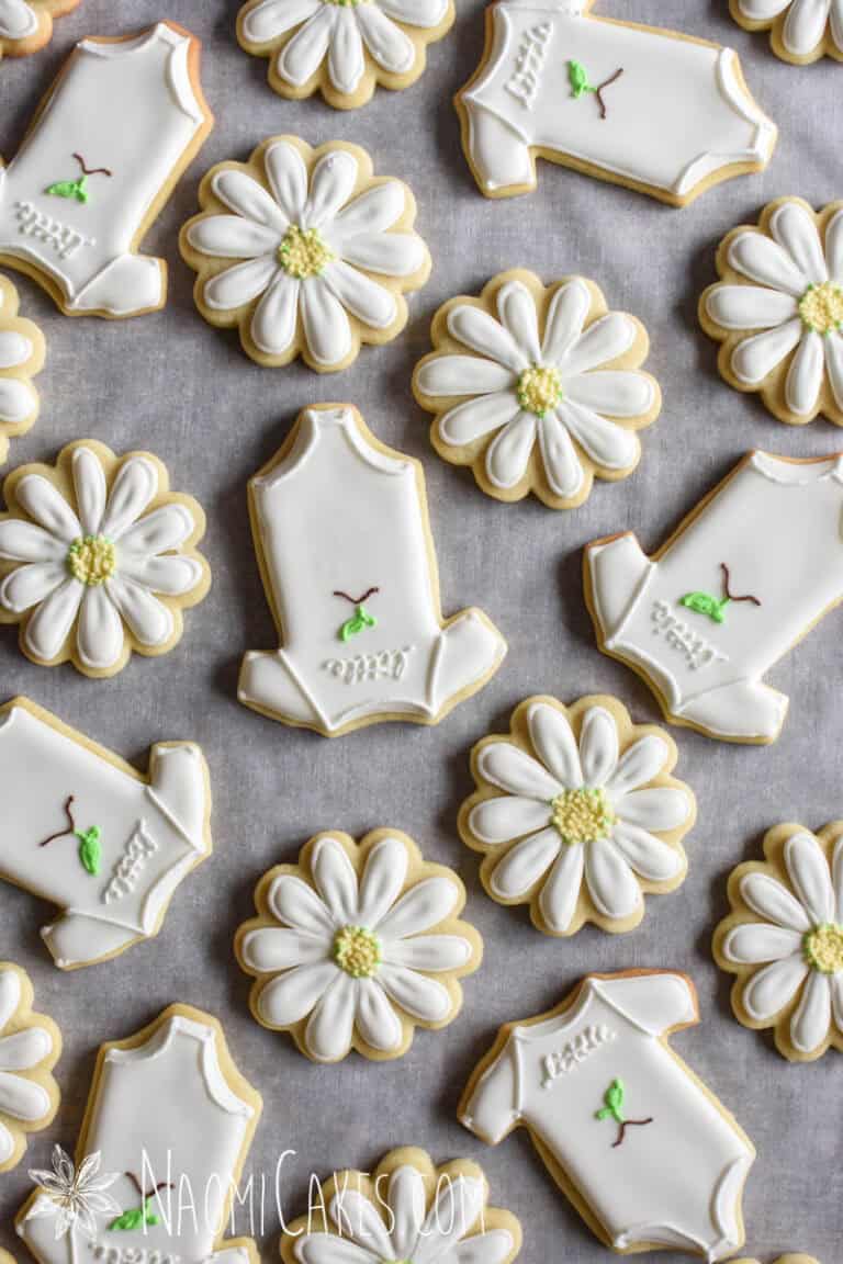 daisy and onesie cookies for a baby shower on parchment paper