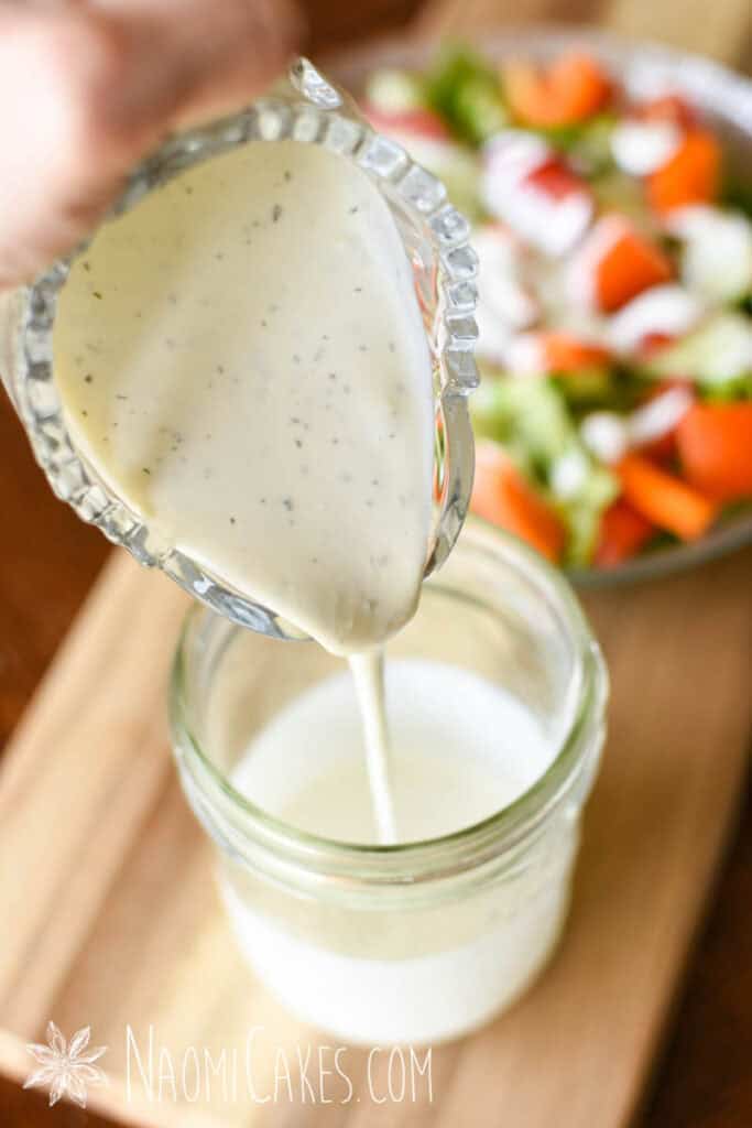 glass pitcher of creamy yogurt salad dressing pouring into a jar