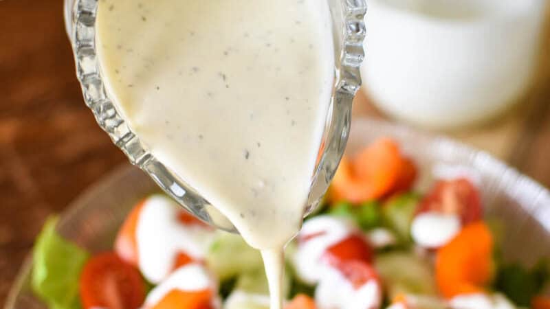 glass pitcher of creamy yogurt salad dressing pouring over a garden salad