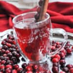overhead view of cranberry apple cider with cranberries and a cinnamon stick on a silver tray