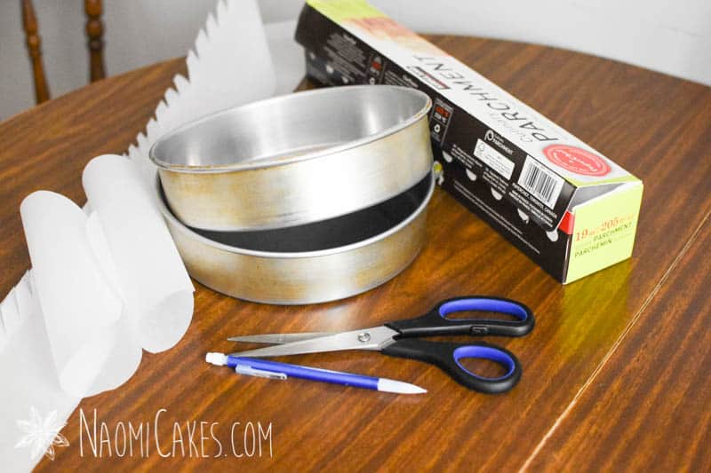 cake pans, scissors, parchment paper, pencil and a wooden table