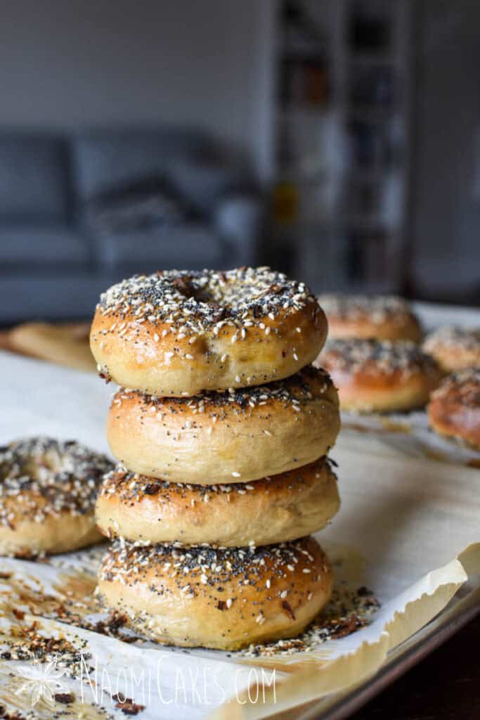 a stack of homemade sourdough everything bagels amidst other bagels on parchment
