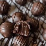 a dark chocolate truffle sitting on top of rows of more truffles with a bite taken out of it, exposing a creamy centre