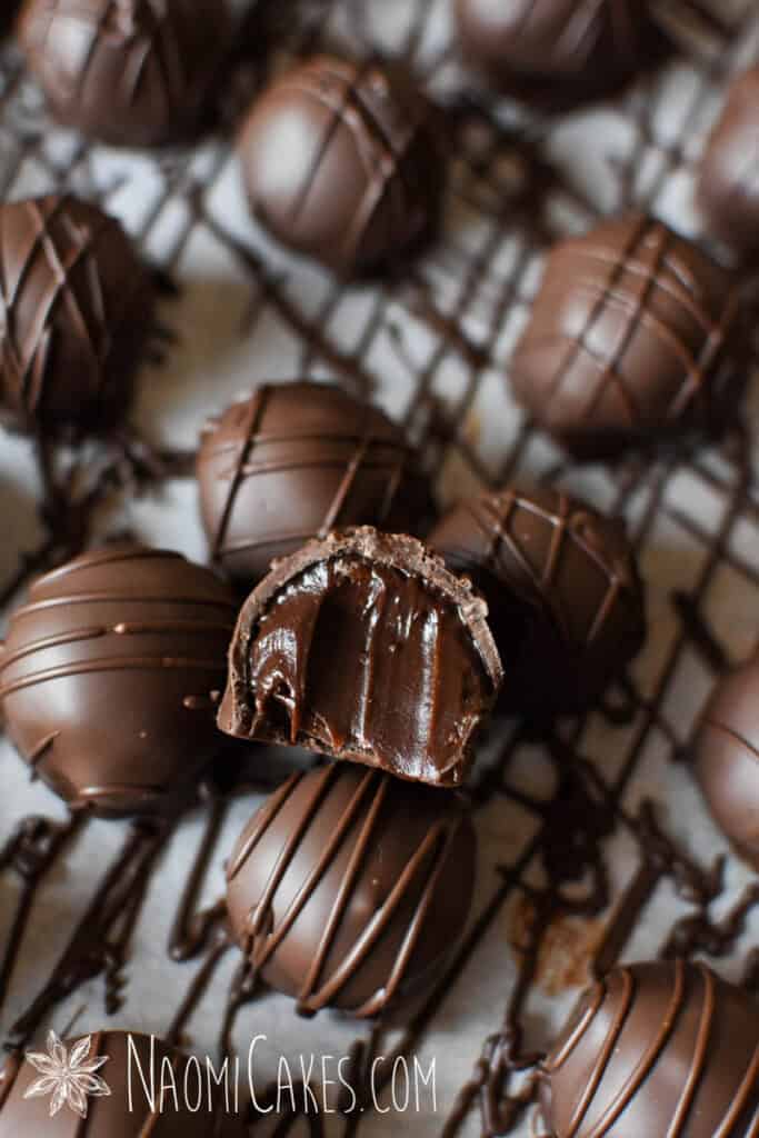a dark chocolate truffle sitting on top of rows of more truffles with a bite taken out of it, exposing a creamy centre
