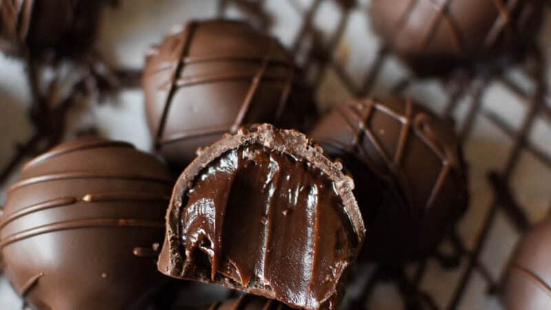 a dark chocolate truffle sitting on top of rows of more truffles with a bite taken out of it, exposing a creamy centre