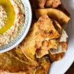 close up overhead view of a large round plate with a bowl of hummus and pita chips