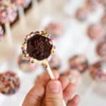 a hand holding a sprinkle covered chocolate cake pop with a bite taken out to show in the inside