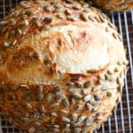 close up of a sourdough pumpkinseed bread loaf on a cooling rack