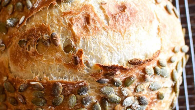 close up of a sourdough pumpkinseed bread loaf on a cooling rack