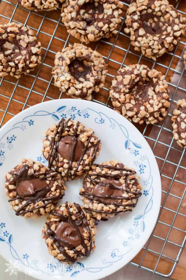 chocolate hazelnut thumbprint cookies drizzled with chocolate on a cooling rack
