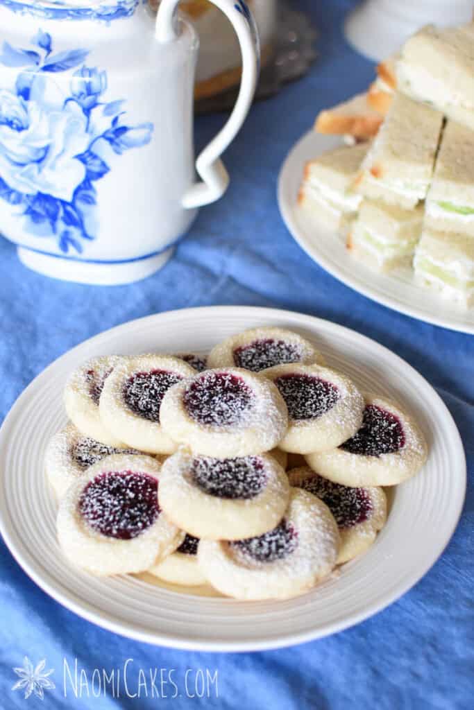 gluten-free shortbread jam thumbprint cookies on a plate on a table with a tea pot and sandwiches in the background