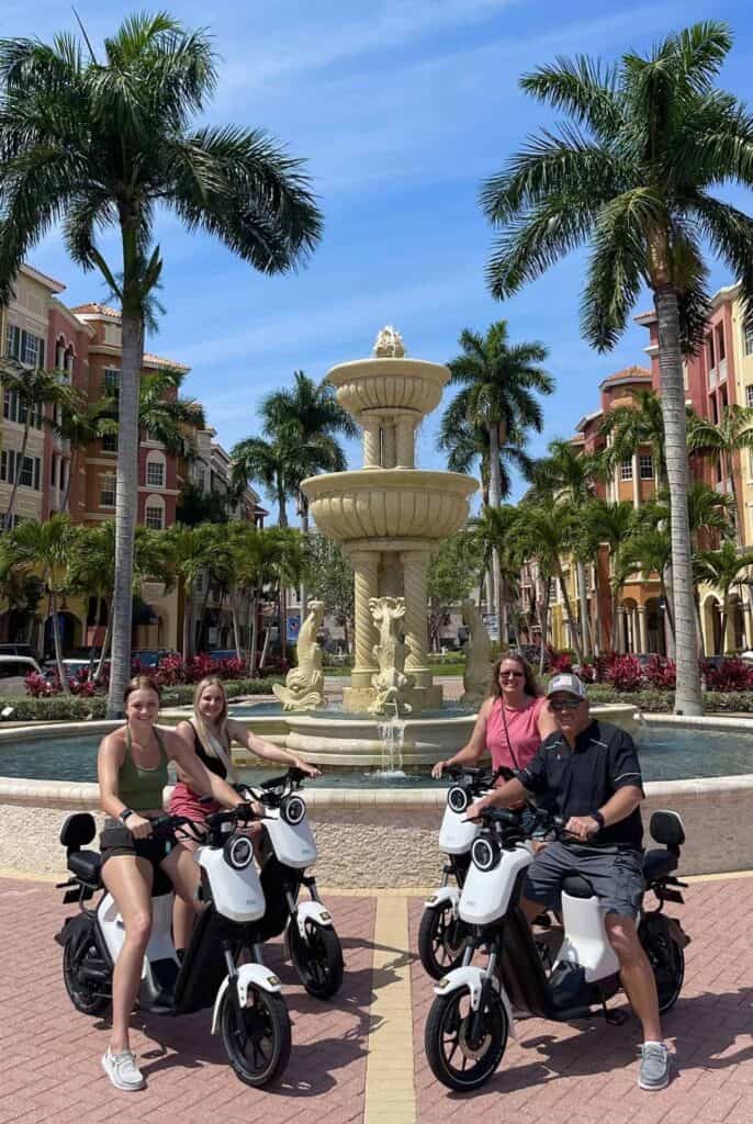 Four guests on electric mopeds beside the Bayfront fountain in Naples