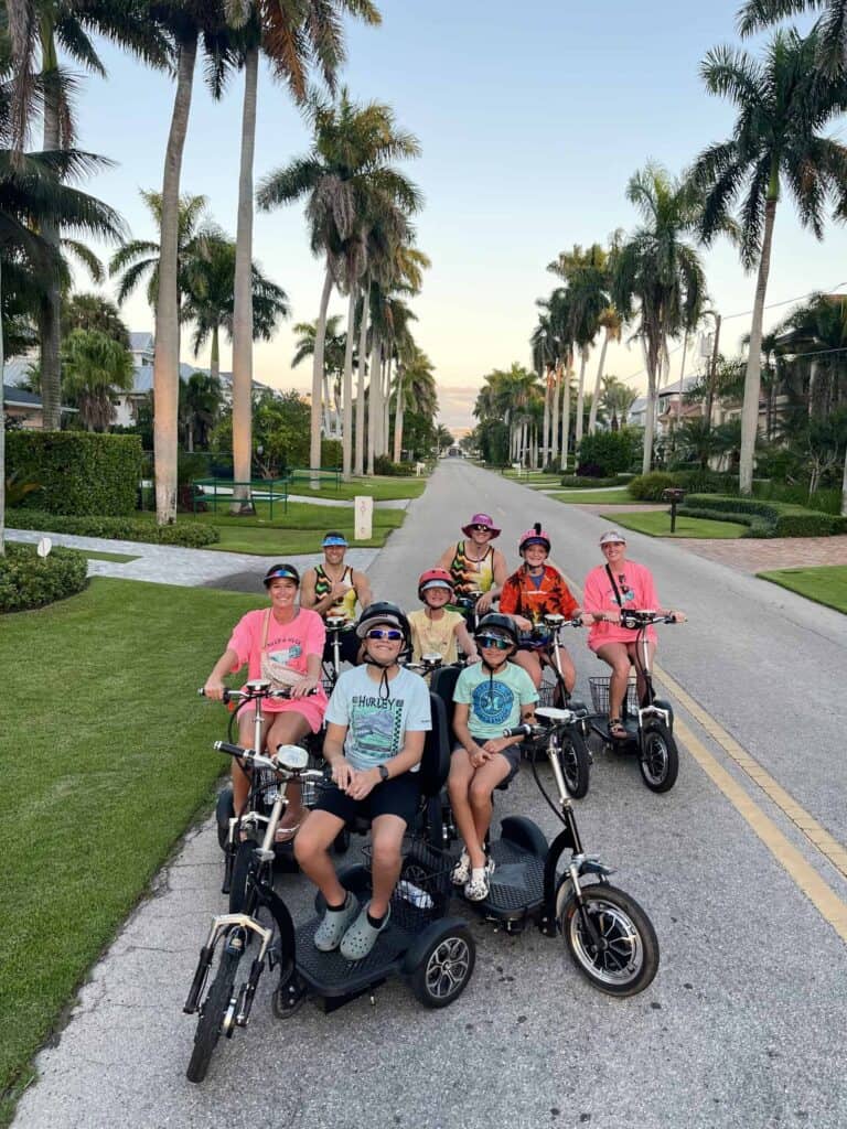 A family posing on electric trikes along a palm-lined Old Naples street