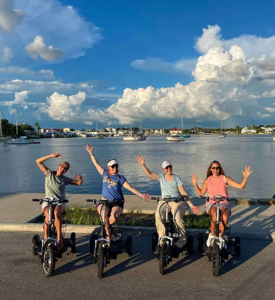 Friends on electric trikes beside Naples Bay and sailboats