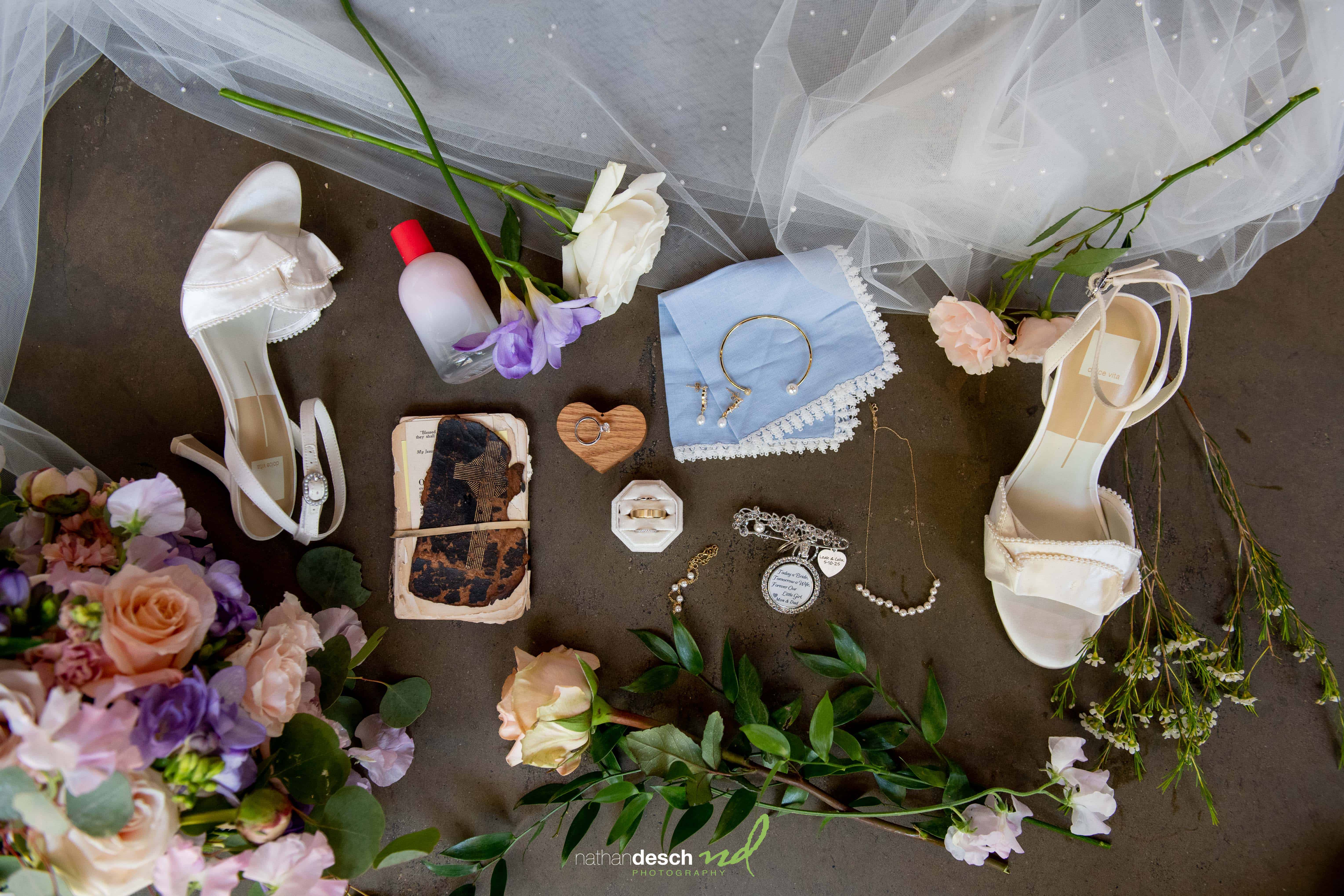 Flat lay of white bridal heels, flowers, jewelry, and wedding details on dark surface at The Inn at Leola Village.