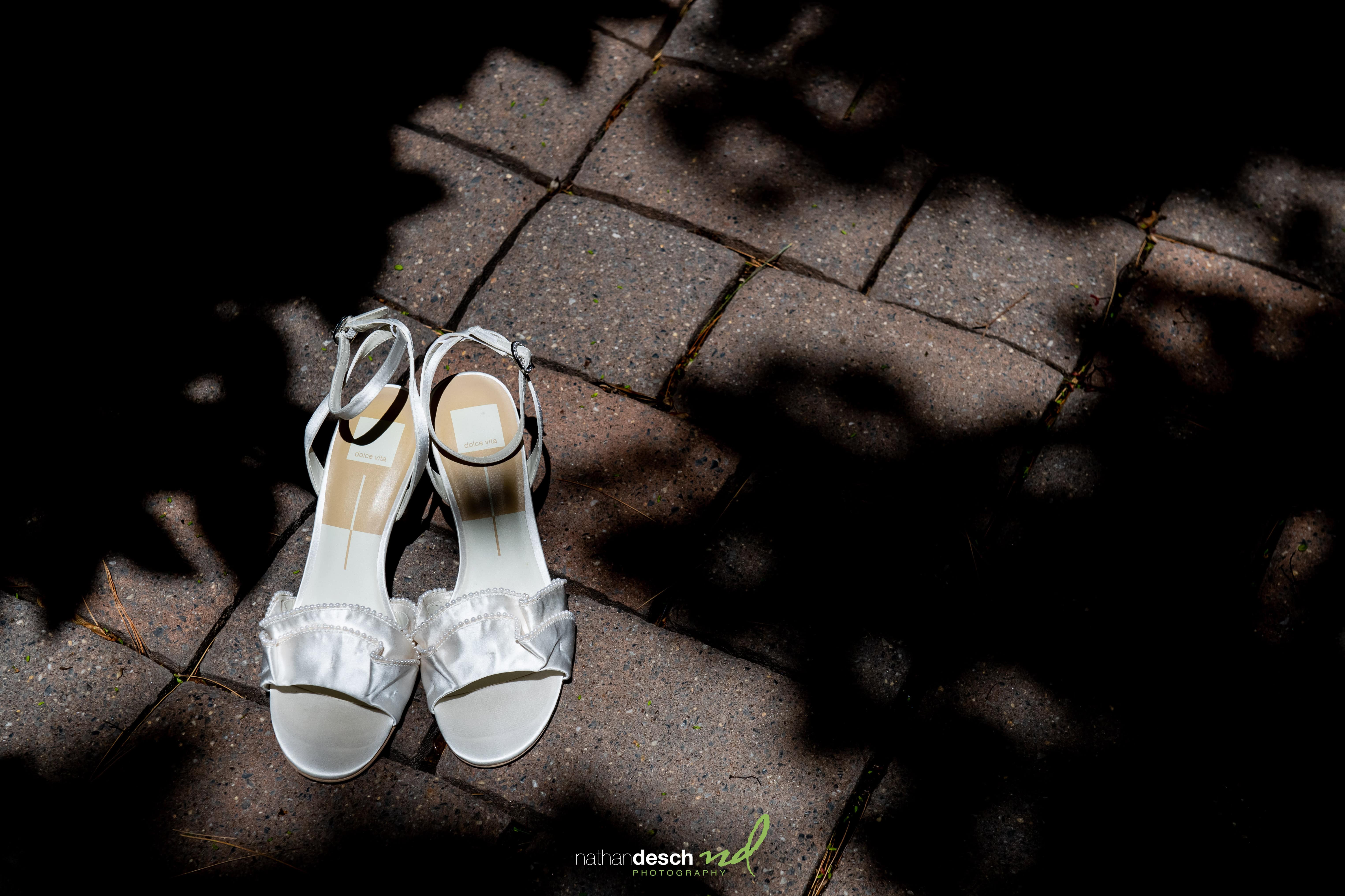 White open-toe bridal heels with ankle straps on sunlit brick at The Inn at Leola Village, elegant wedding shoes.
