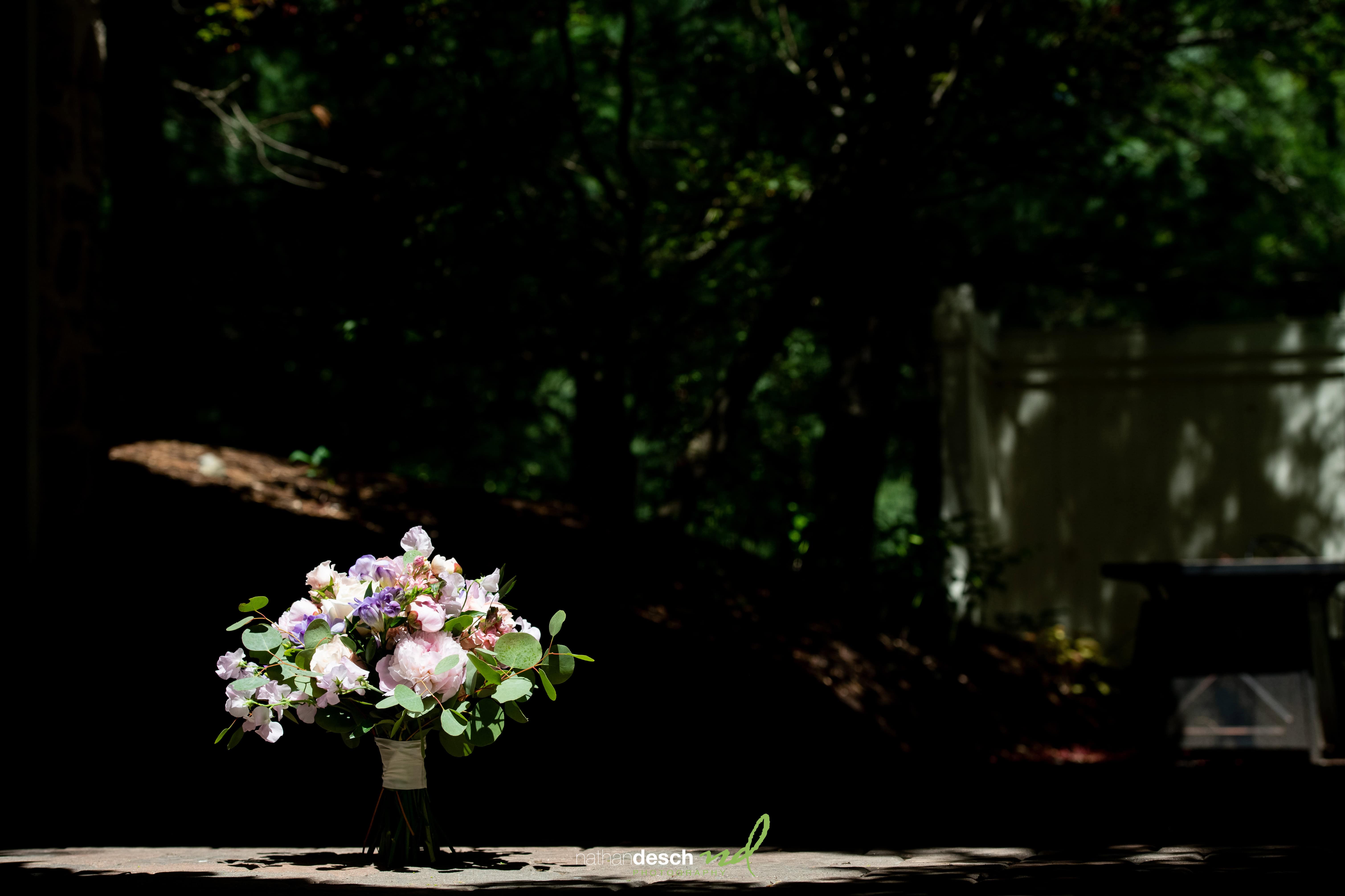 Pastel wedding bouquet on sunlit table at Inn at Leola Village, surrounded by greenery—ideal for a spring outdoor ceremony.