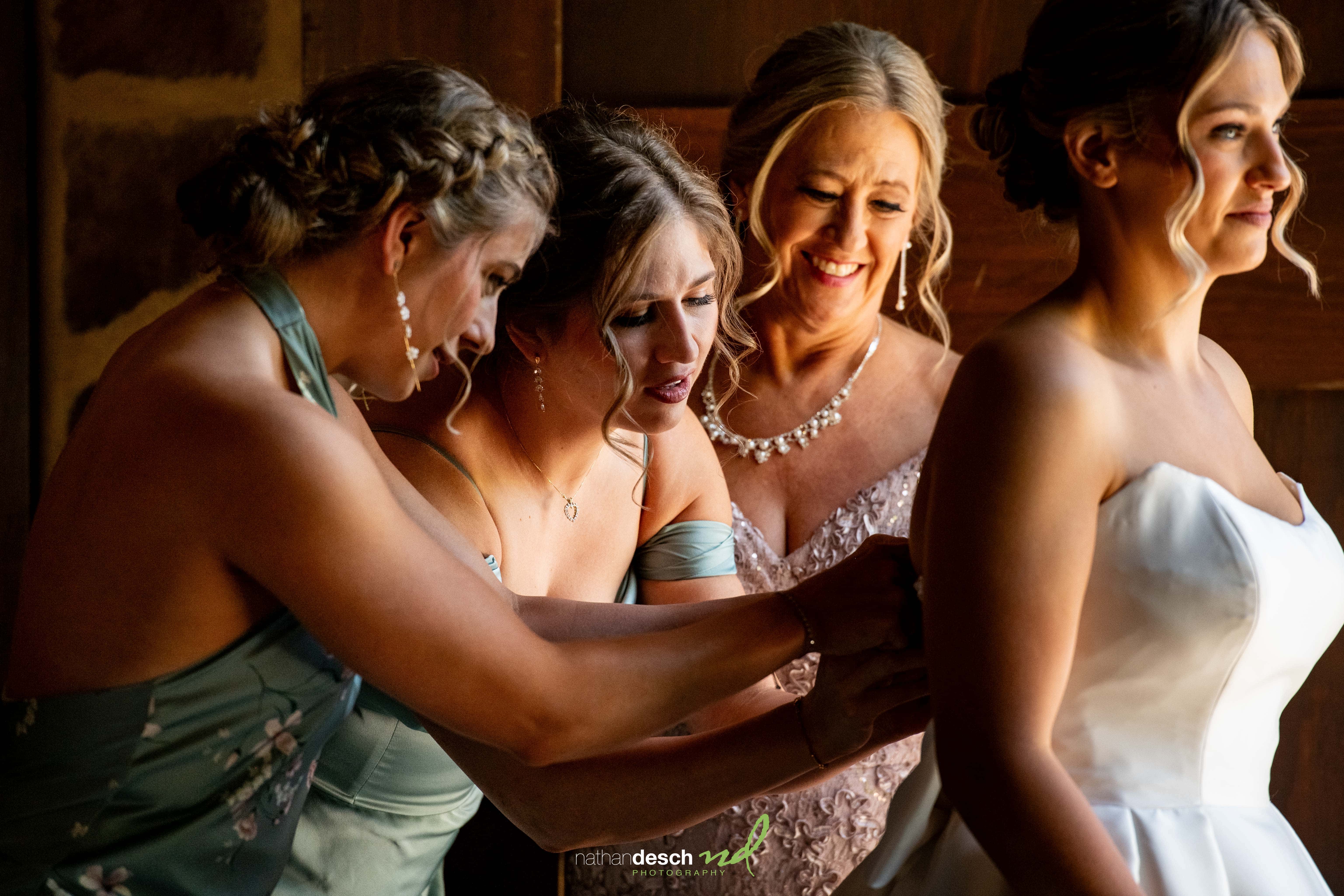 Bride smiling as bridesmaids button her wedding dress in warmly lit suite at The Inn at Leola Village.