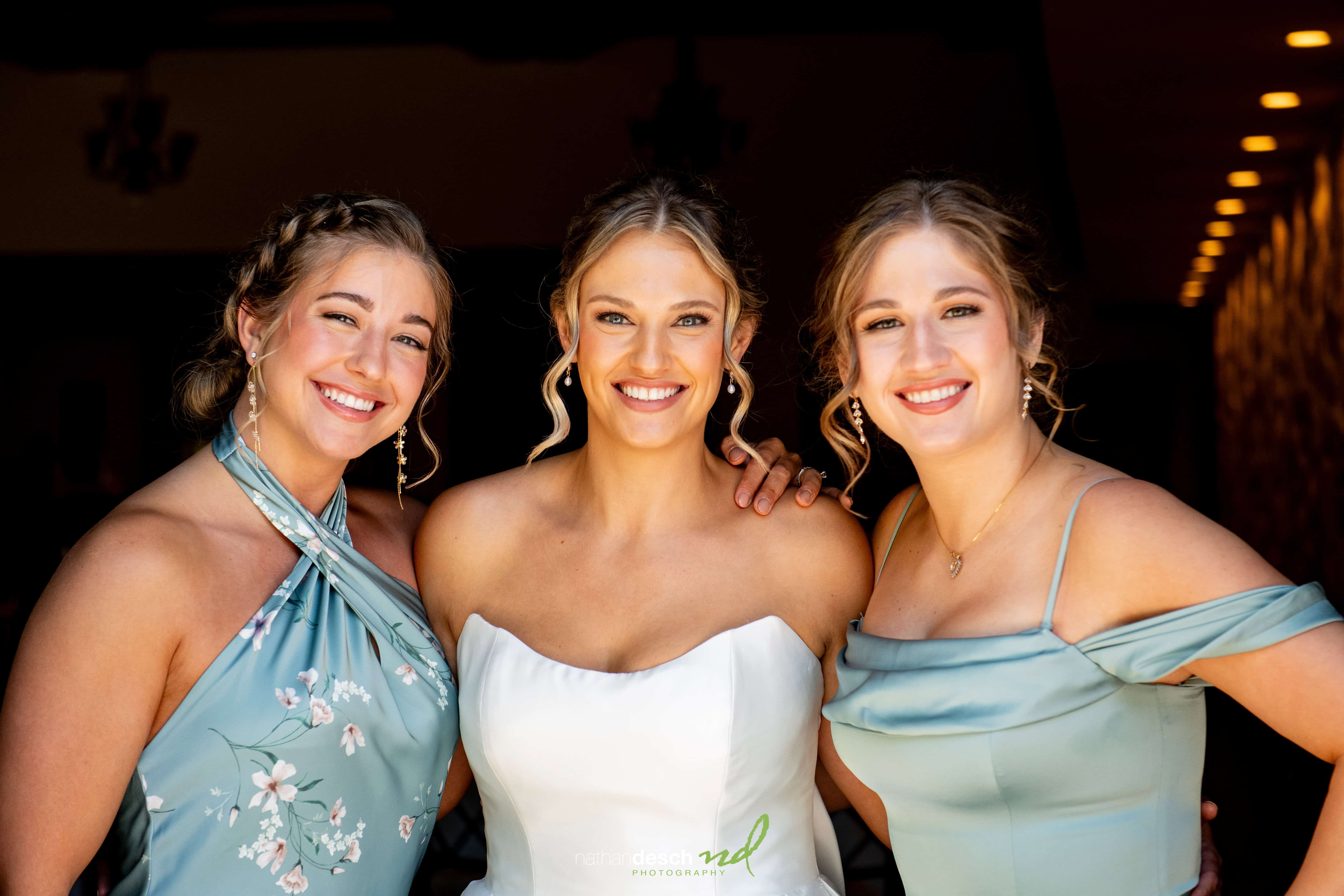 Bride in strapless white gown with bridesmaids in blue floral dresses smiling at Inn at Leola Village spring wedding.