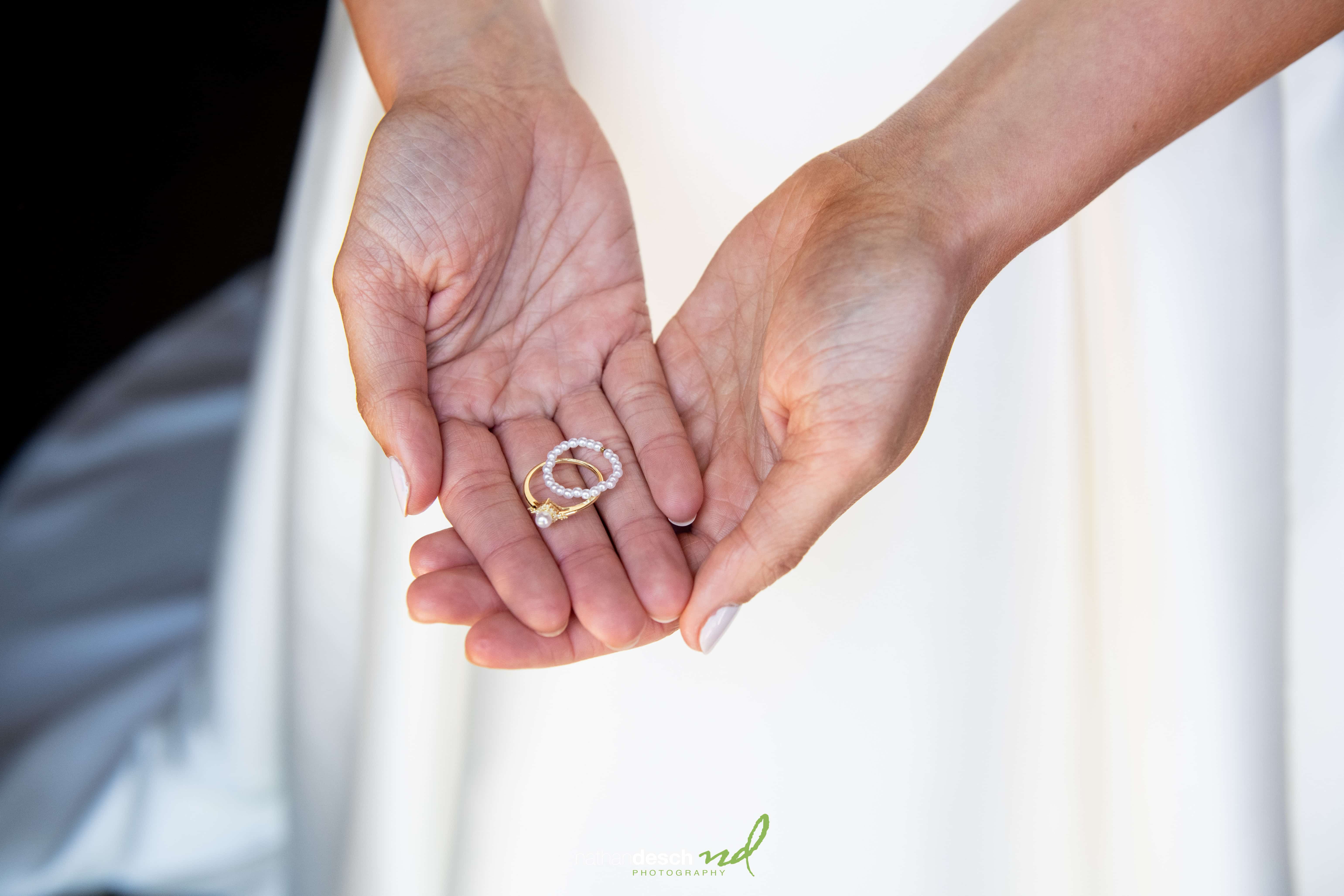 Bride in white dress holding wedding rings and pendant in her hands, softly lit at The Inn at Leola Village wedding.
