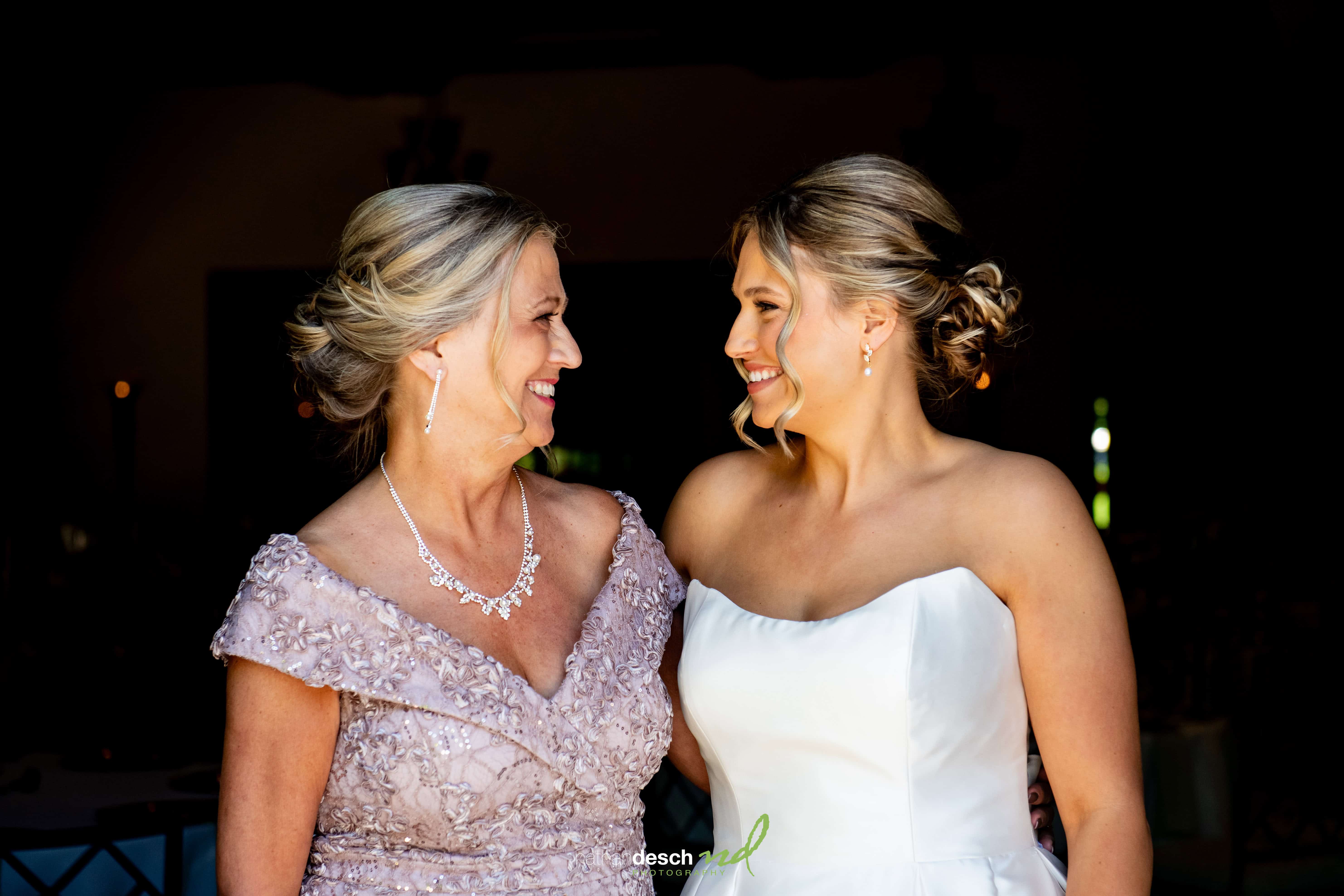 Two brides, one in lavender and one in a white dress, smile and embrace at their elegant Inn at Leola Village wedding.