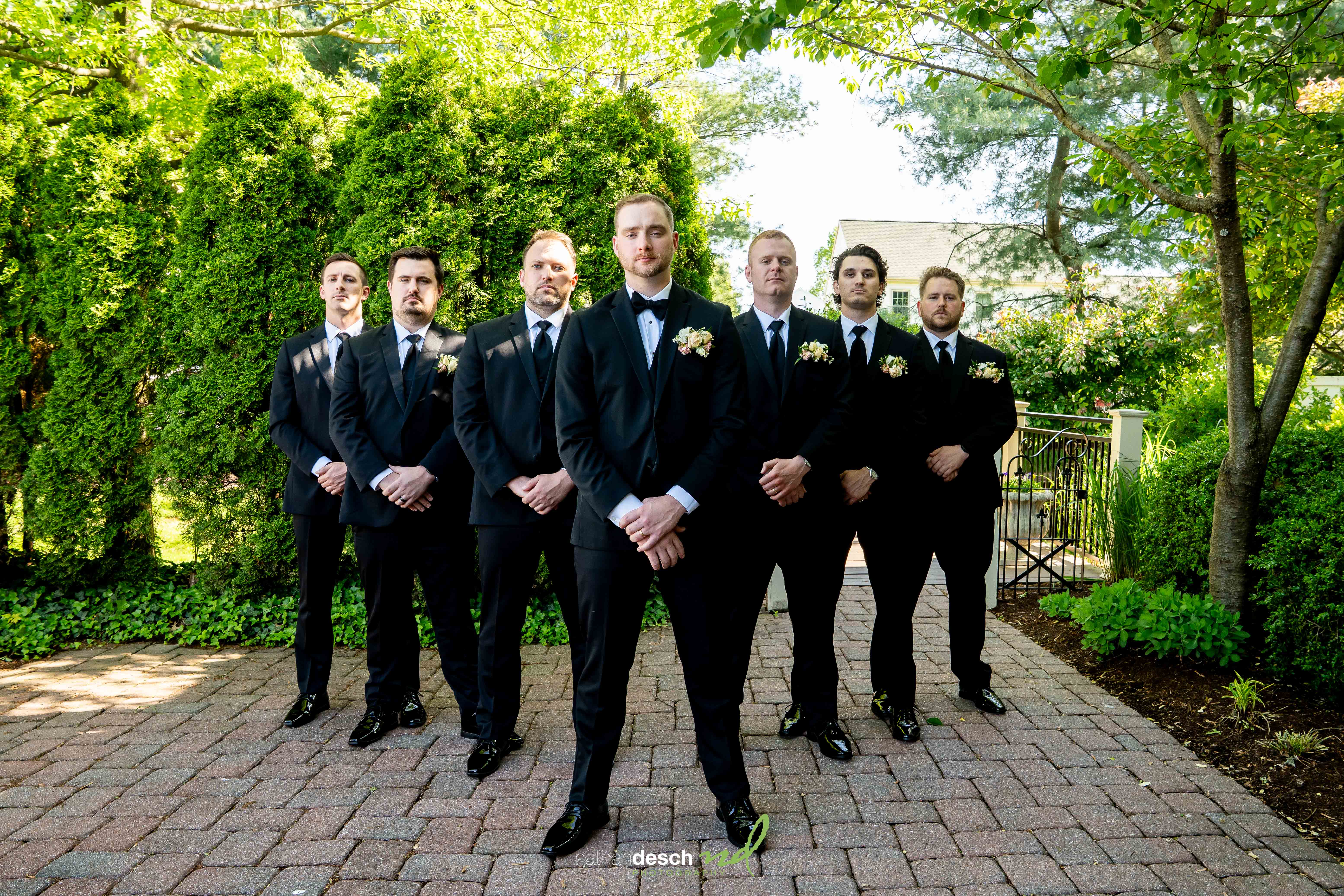 Groomsmen in black tuxedos with bow ties pose outdoors on a sunny day at The Inn at Leola Village wedding.