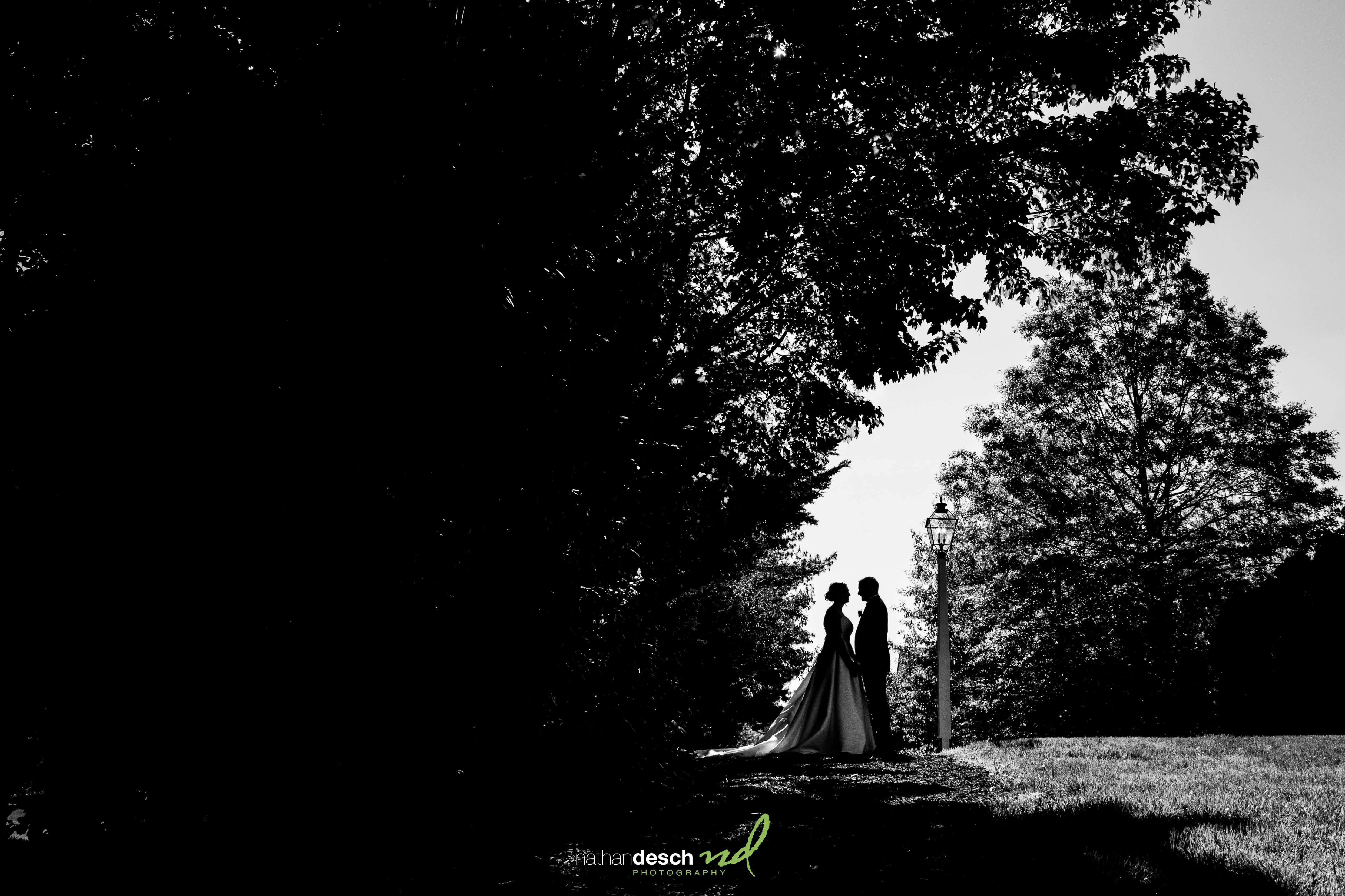 Bride and groom silhouette by a lamp post at the Inn at Leola Village, surrounded by trees and spring wedding light.