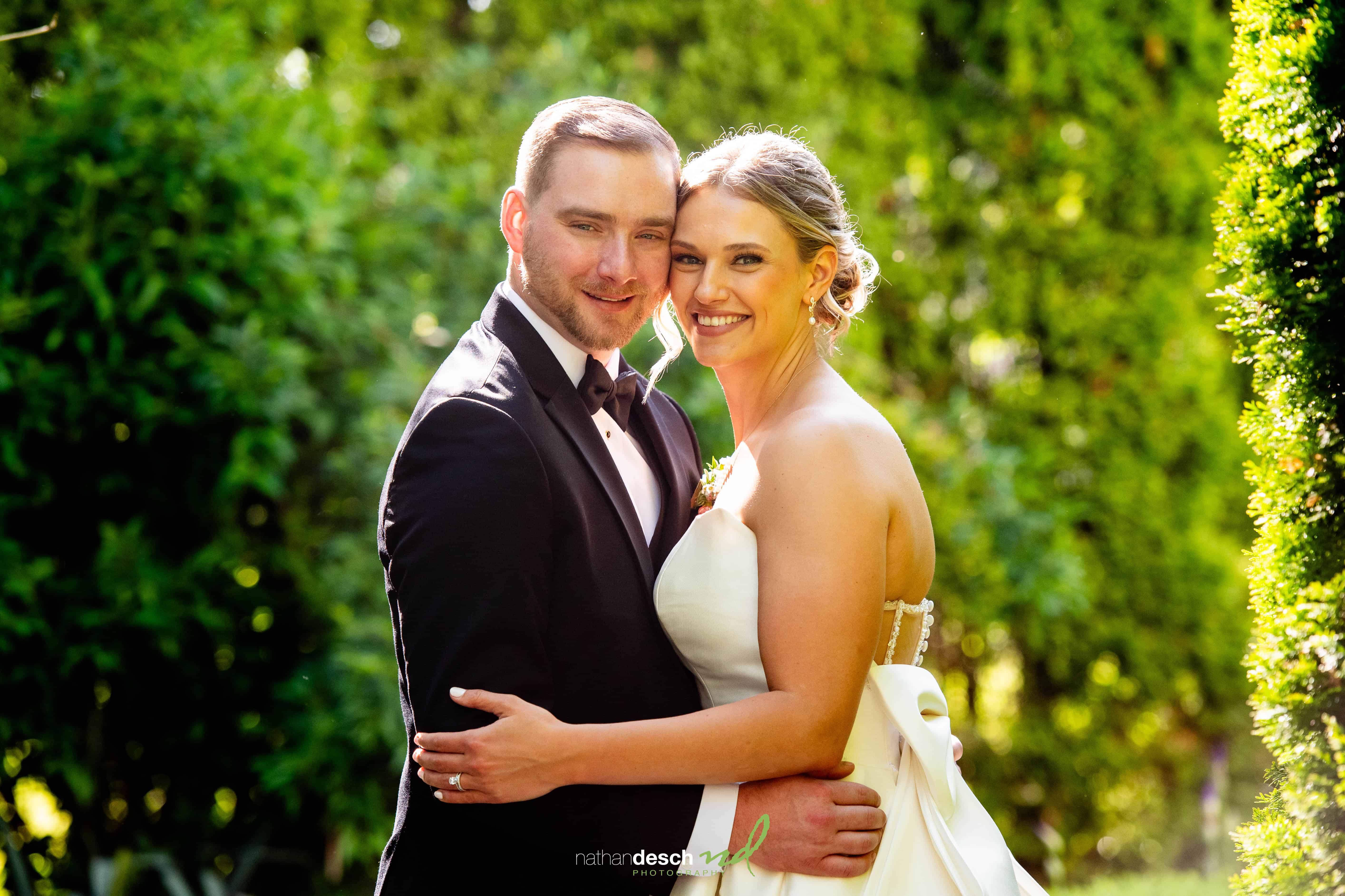 Bride and groom embrace outdoors in elegant wedding attire, surrounded by greenery at The Inn at Leola Village spring wedding.