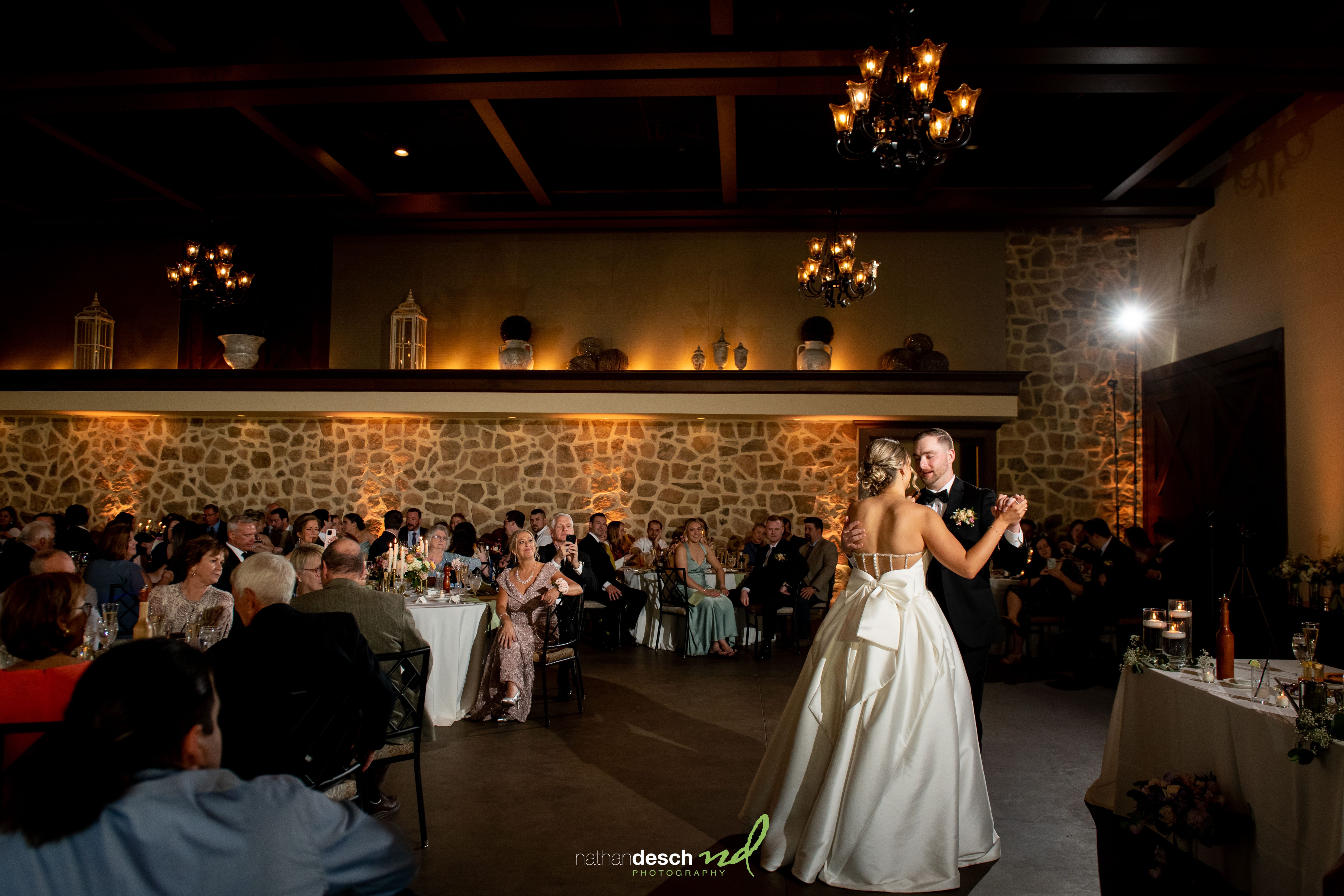 Bride and groom share first dance under chandeliers at The Inn at Leola Village wedding, guests smiling in elegant hall.