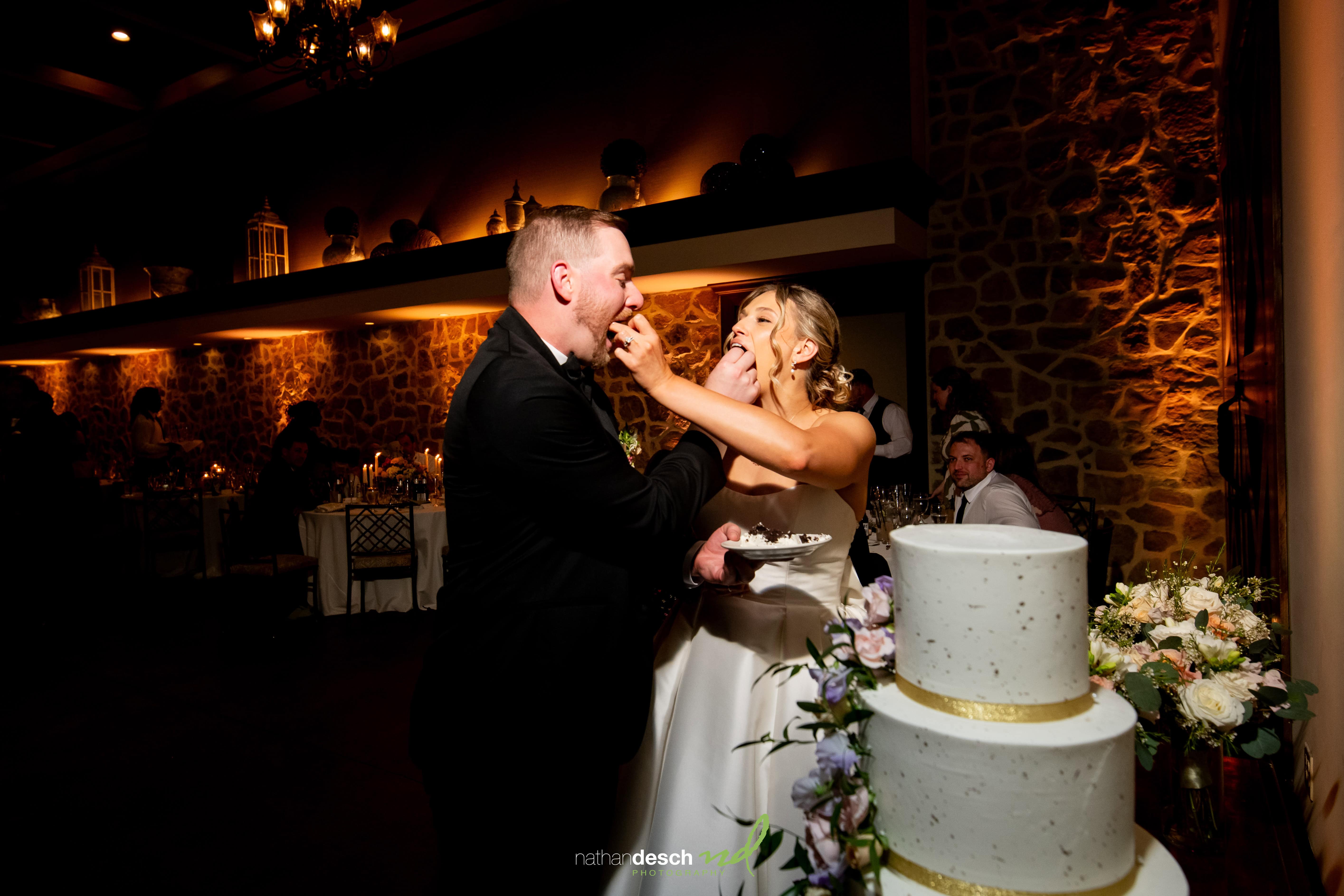 Bride and groom laughing while feeding each other cake at elegant Inn at Leola Village wedding reception with floral cake.