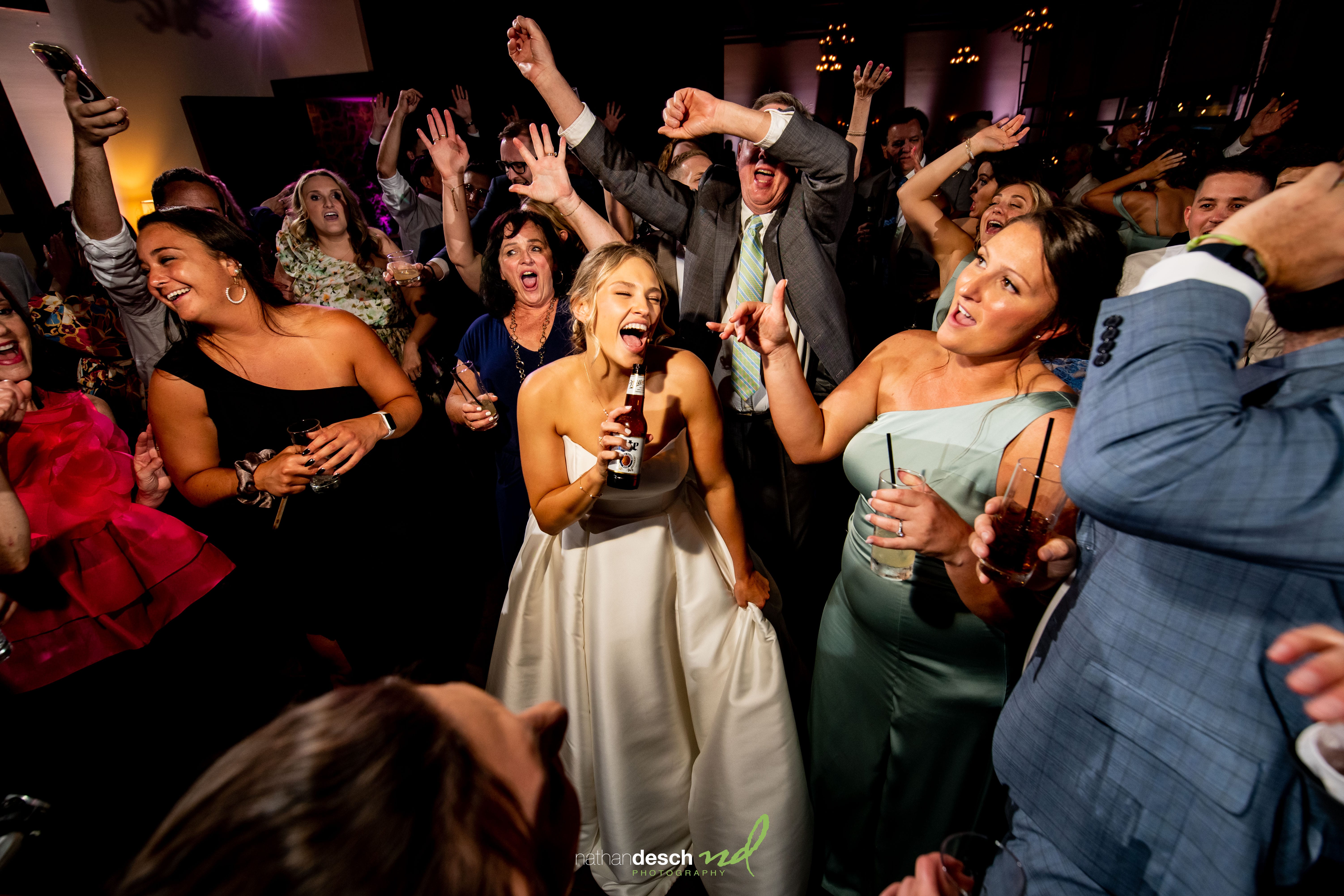 Bride in white gown dancing with friends at joyful wedding reception, guests smiling and celebrating at The Inn at Leola Village.