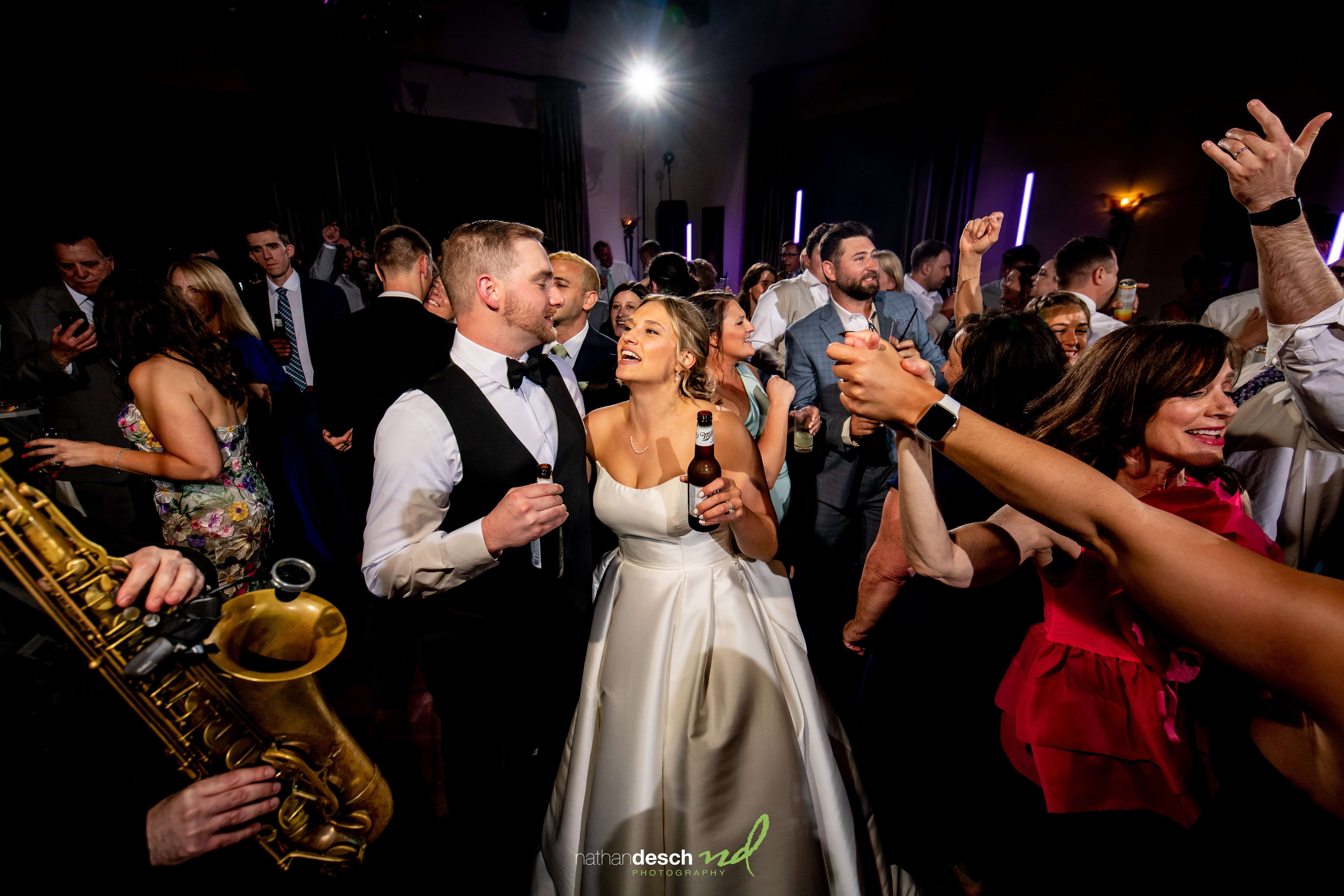 Bride and groom dancing at The Inn at Leola Village wedding, surrounded by guests, colorful lights, and live saxophonist.