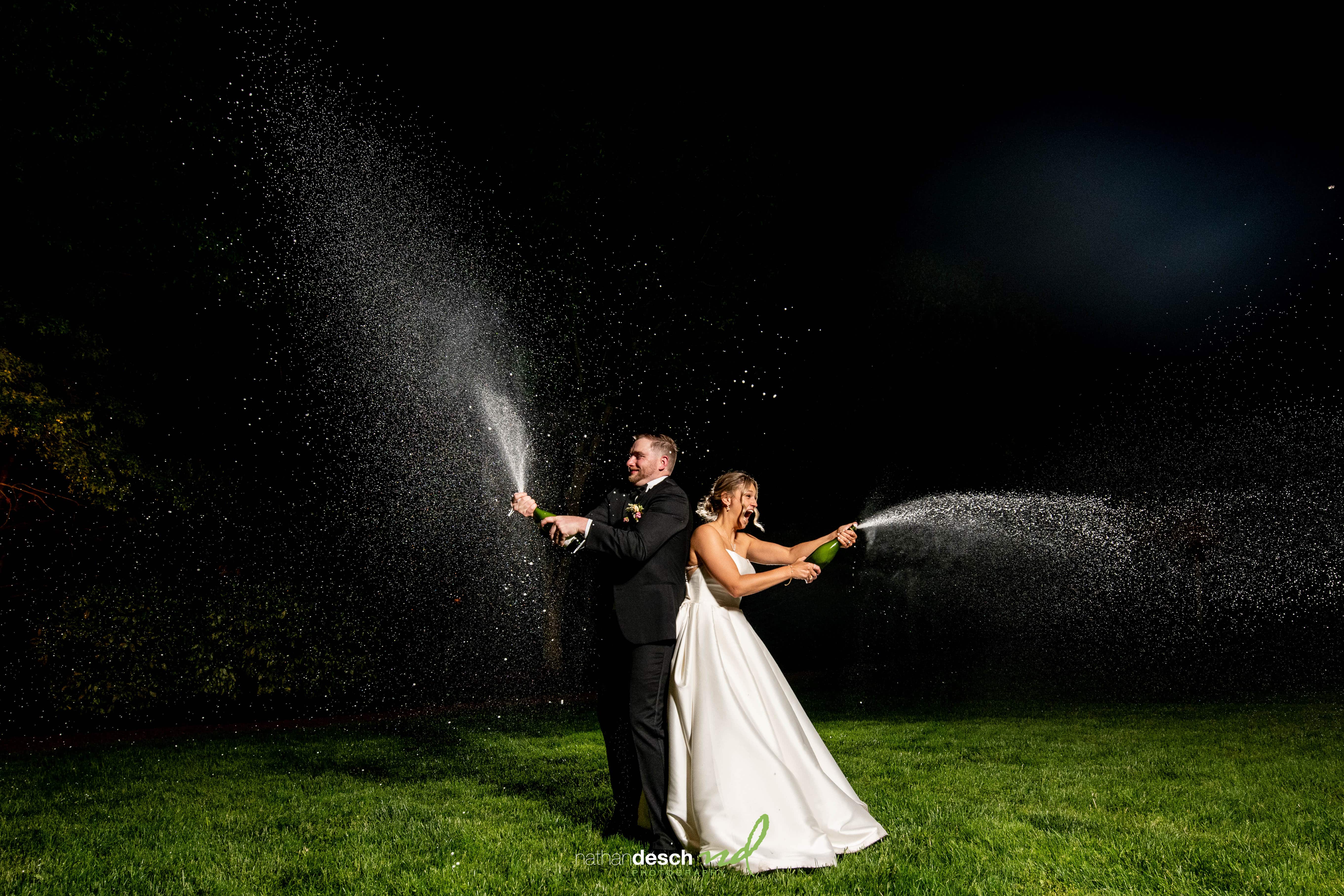 Bride and groom spraying champagne under sparkling lights at night wedding