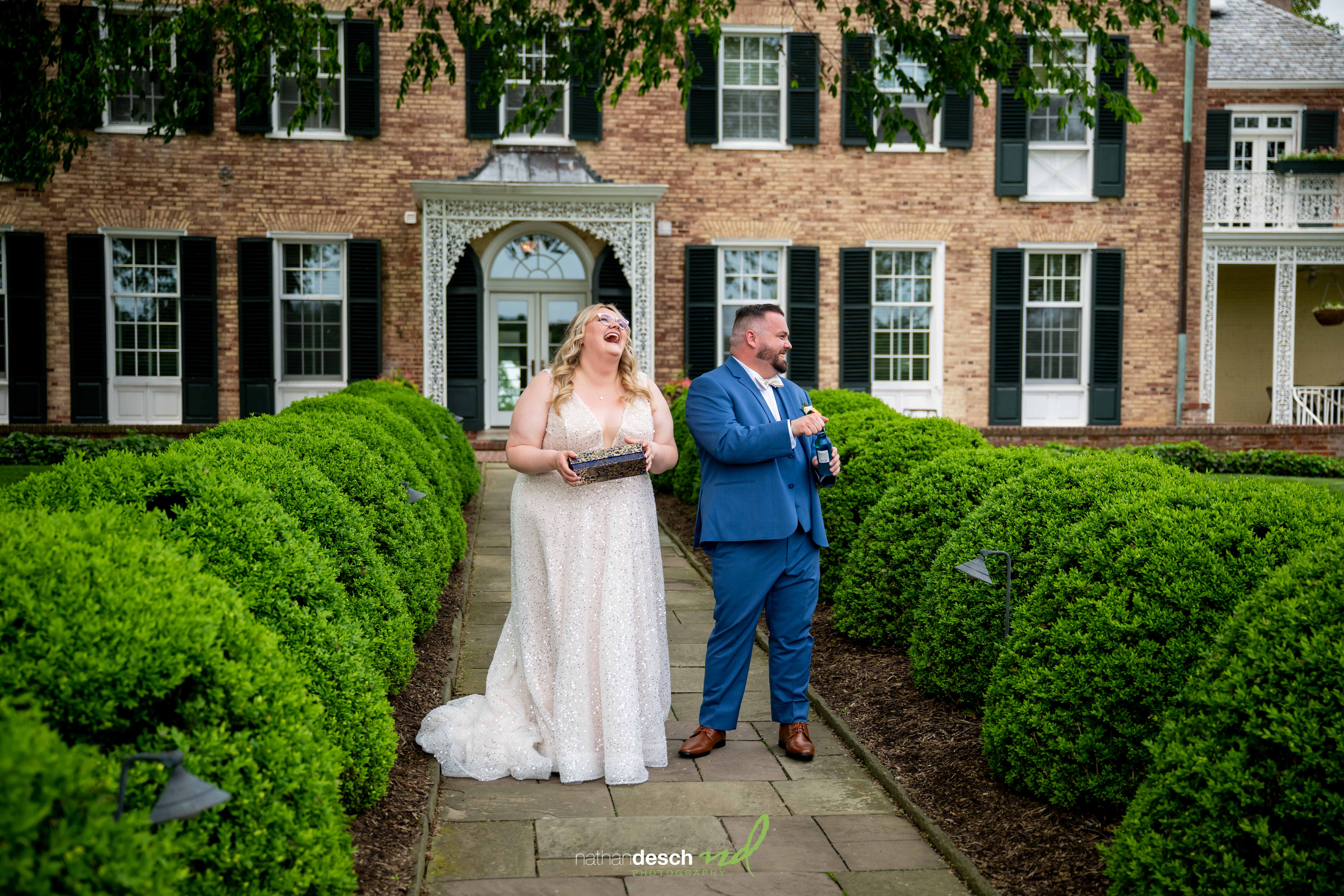 Bride and groom laughing on garden path at Drumore Estate during spring wedding, brick mansion in background.