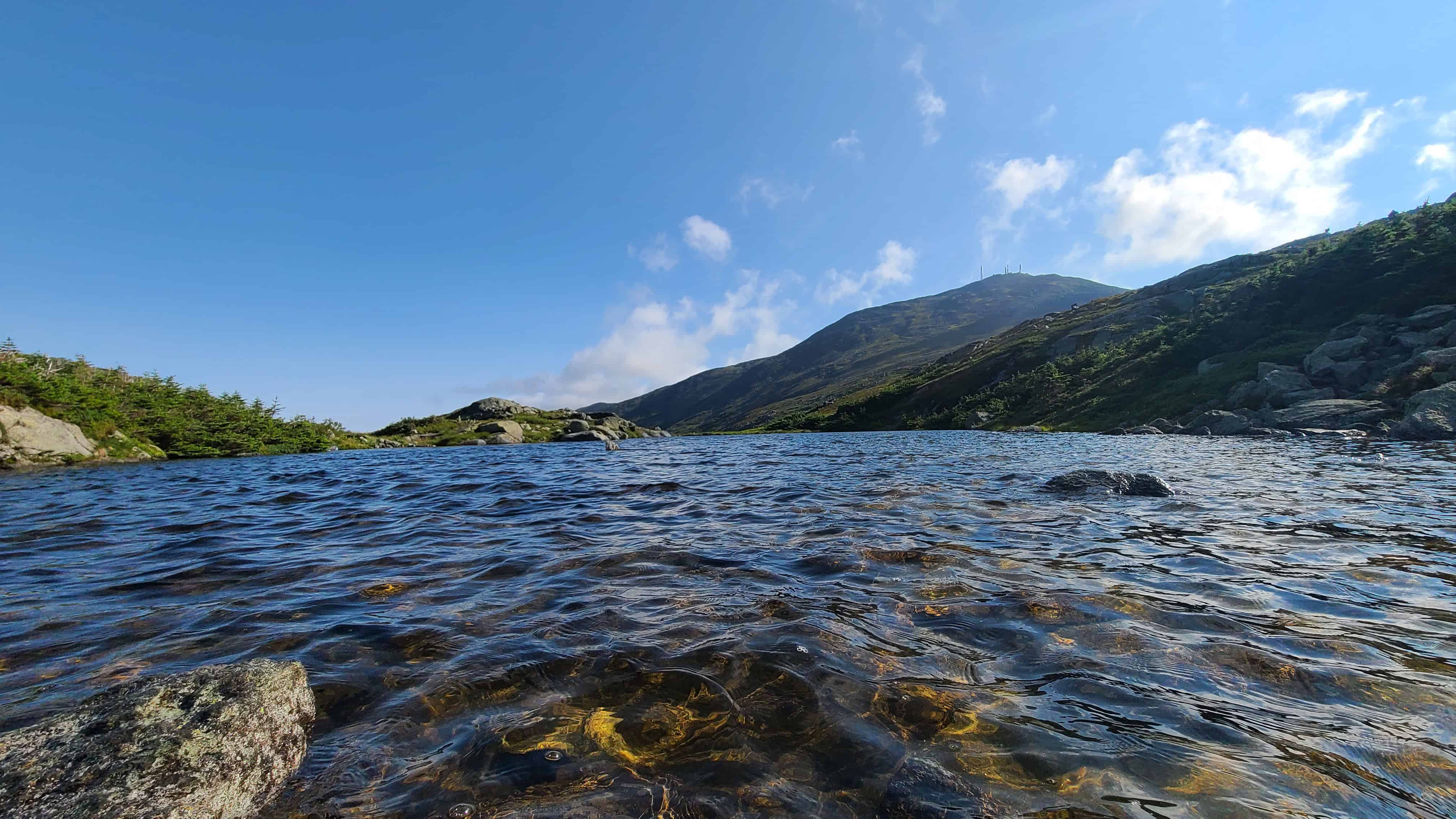 Scenic mountain lake with rippling water, rocky shore, and green hills—romantic White Mountains adventure wedding location.