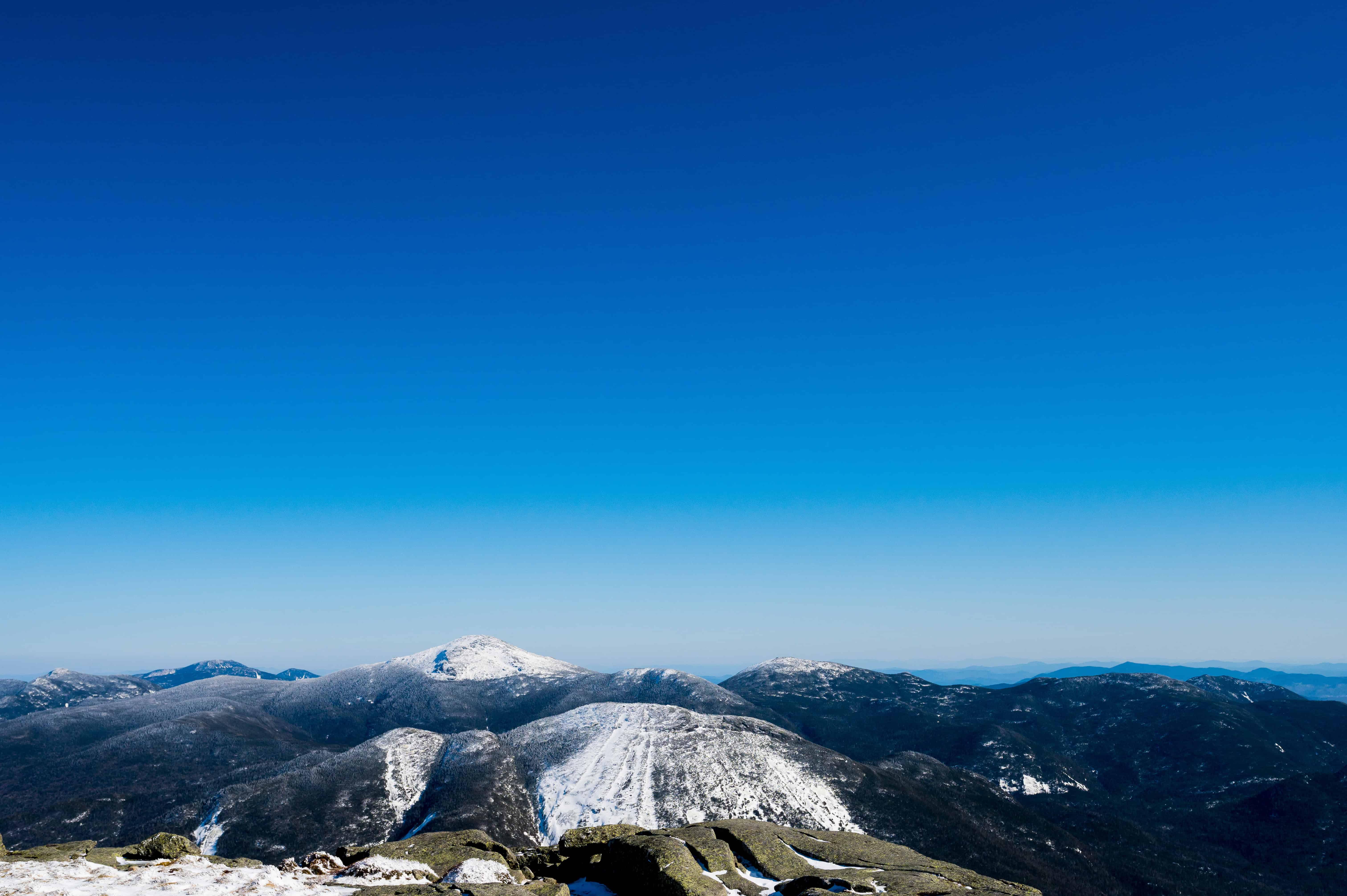 Snow-capped White Mountains under blue sky, rocky foreground—ideal for a Presidential Traverse adventure wedding photo.