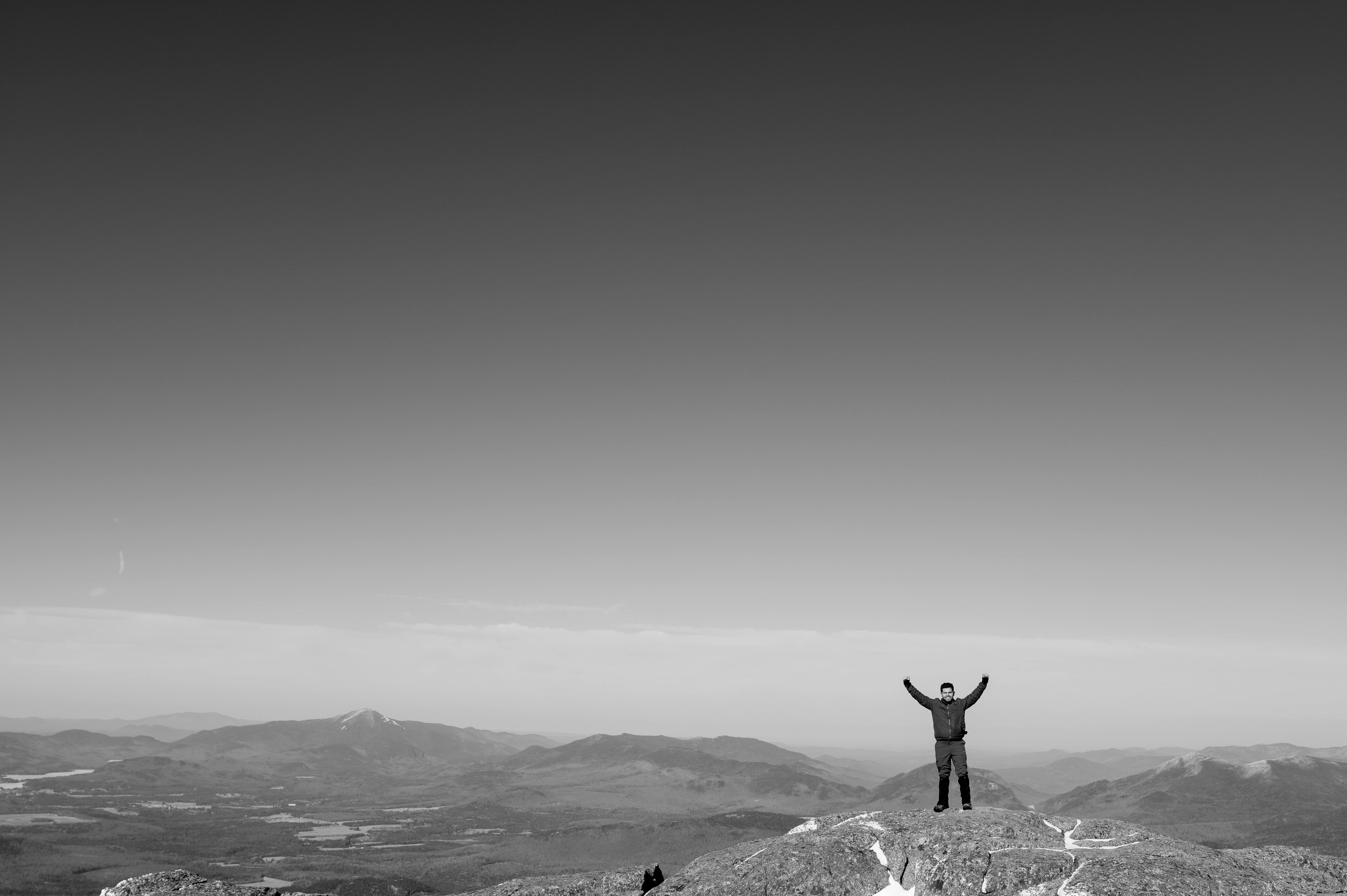 Black and white image of a person celebrating atop a rocky peak in the White Mountains, ideal for adventure wedding photography.