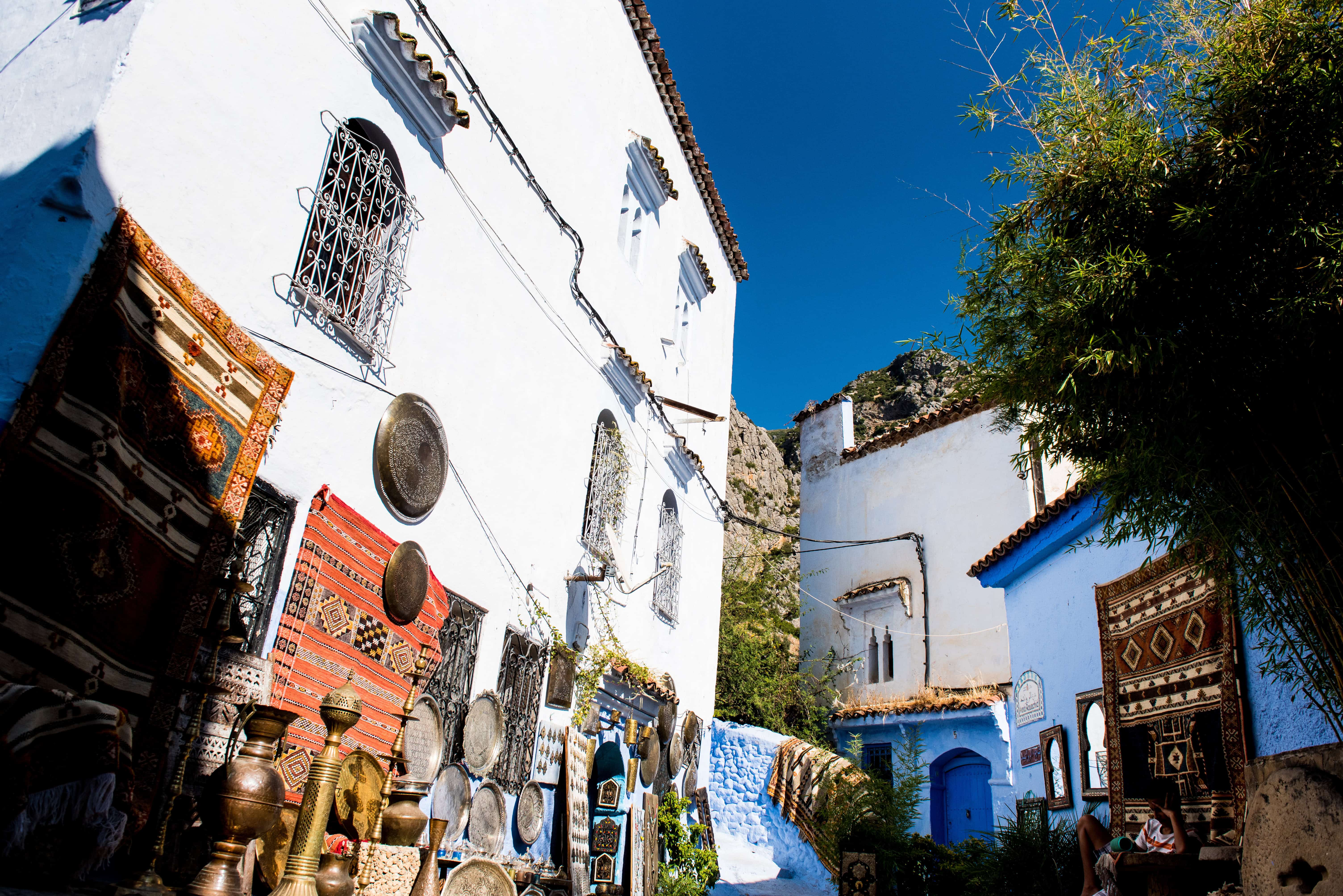 Colorful Chefchaouen street with blue buildings, woven rugs, and pottery—Morocco elopement wedding photography scenery.