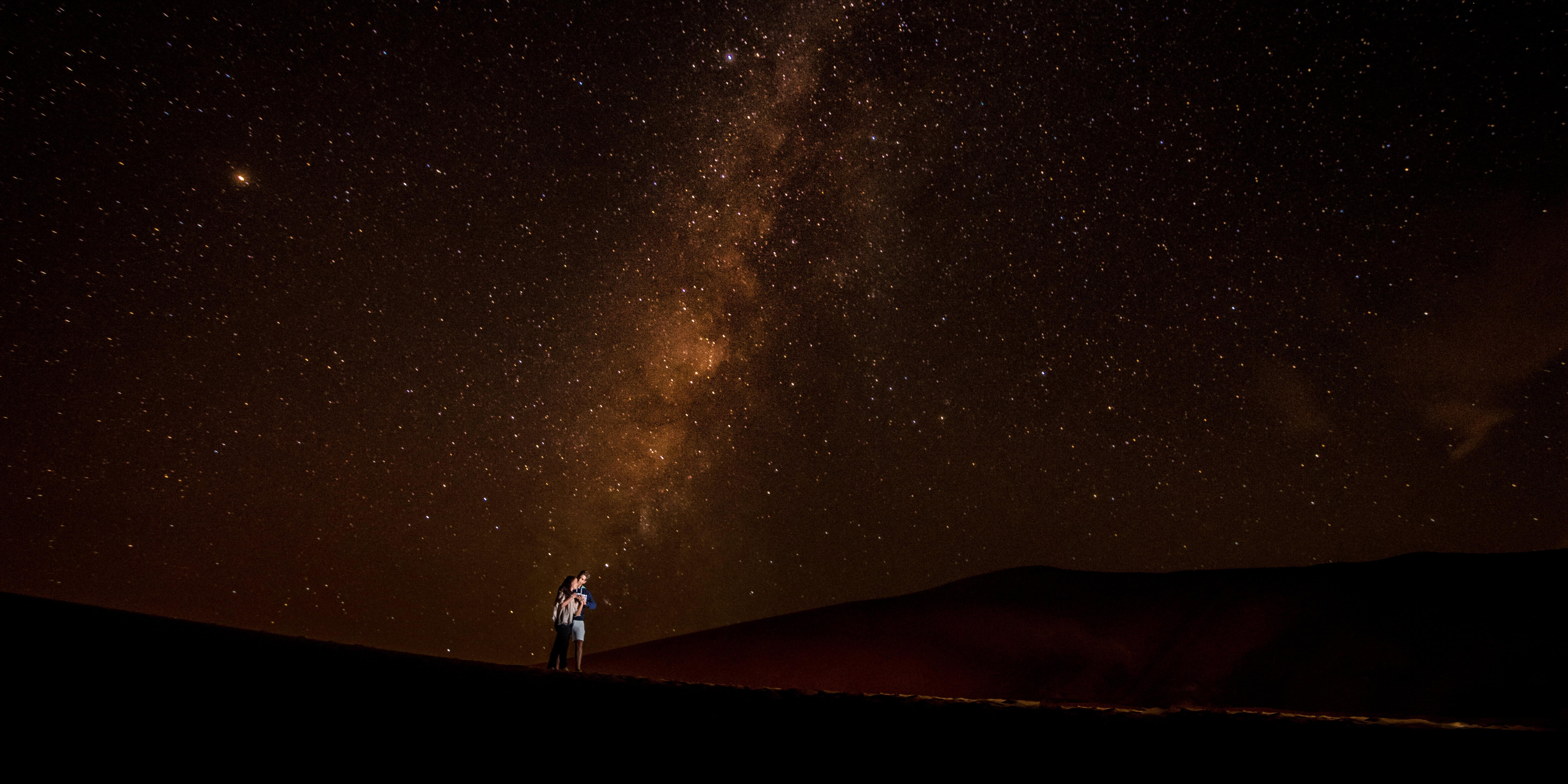 Couple embracing on a Sahara dune under star-filled Milky Way sky, photographed by a Morocco elopement photographer near Marrakech.