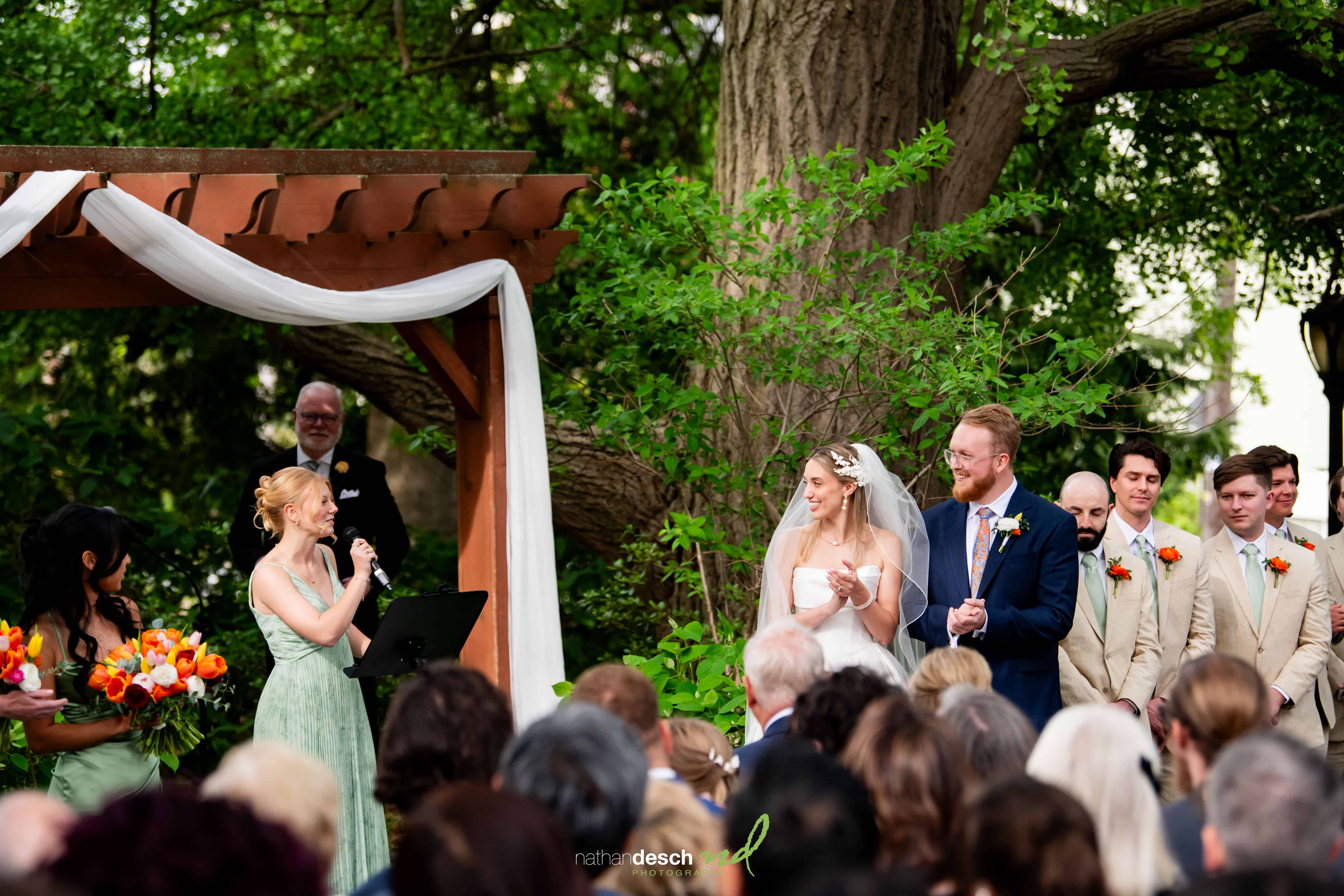 Outdoor wedding at University and Whist Club with smiling bride and groom, bridesmaids with orange bouquets, elegant decor, greenery.