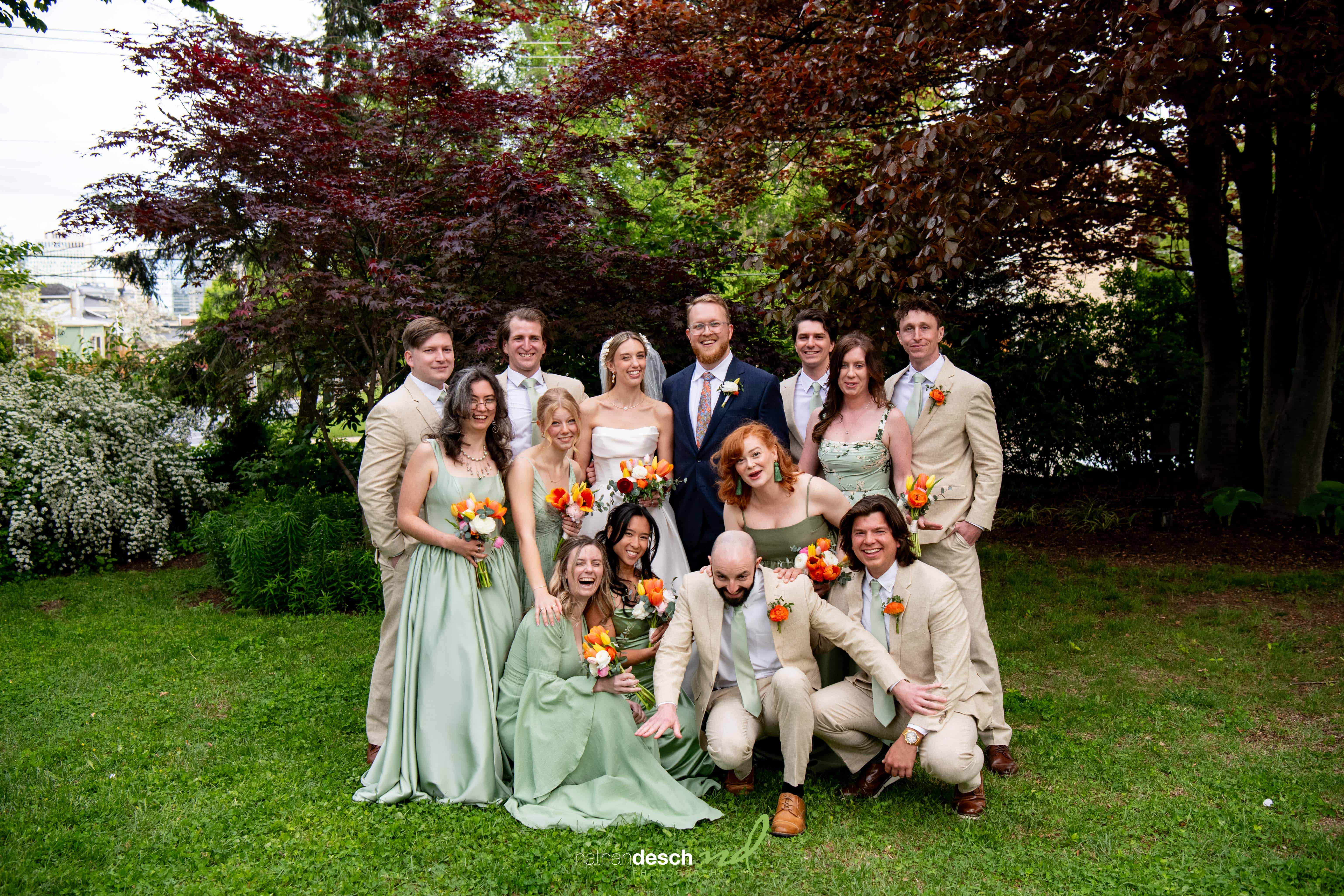 Outdoor wedding party at University and Whist Club, guests in green dresses and tan suits, laughing and holding bouquets.