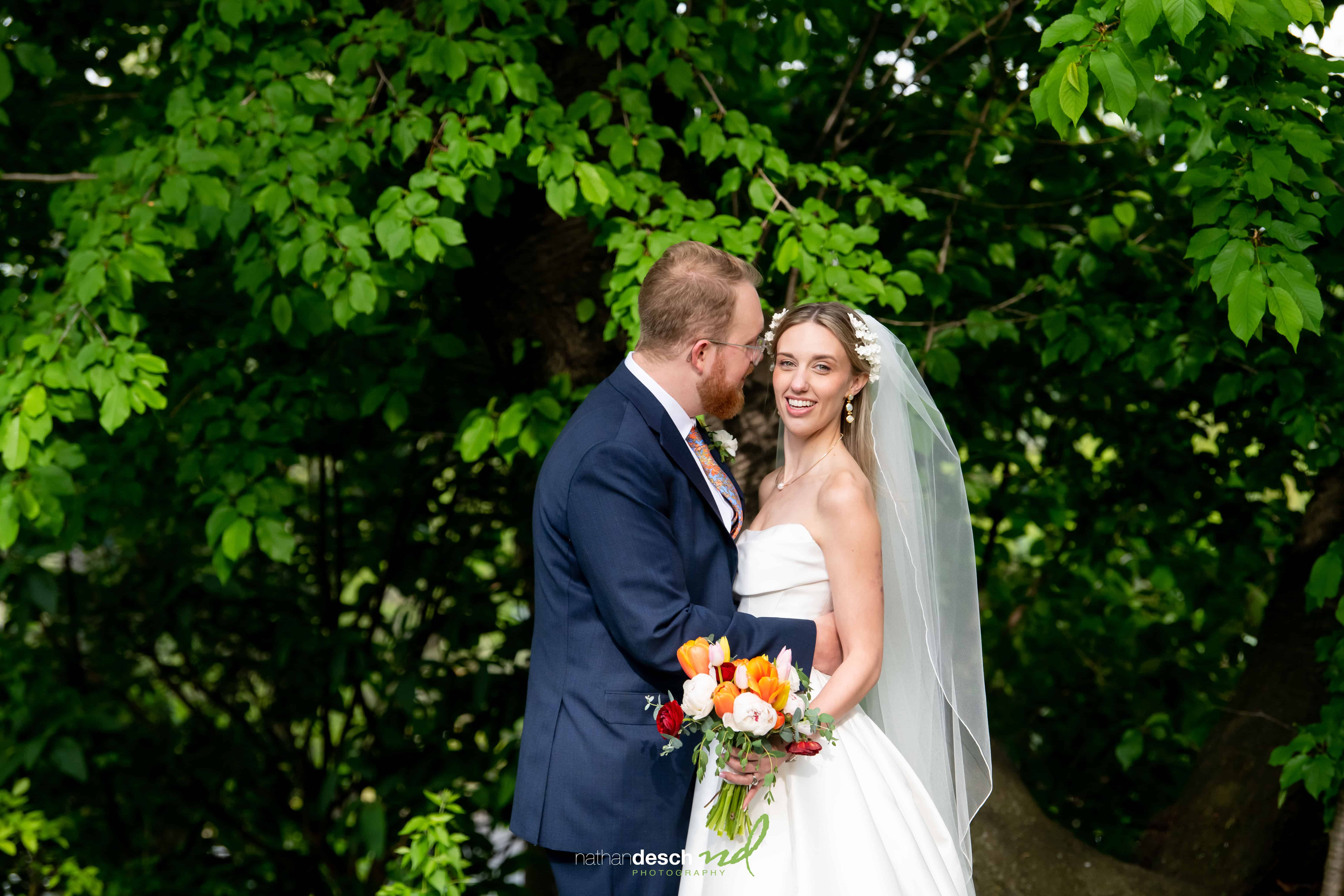 Bride and groom, Garrett and Ashley, smiling outdoors at University and Whist Club Wedding with bouquet and greenery.