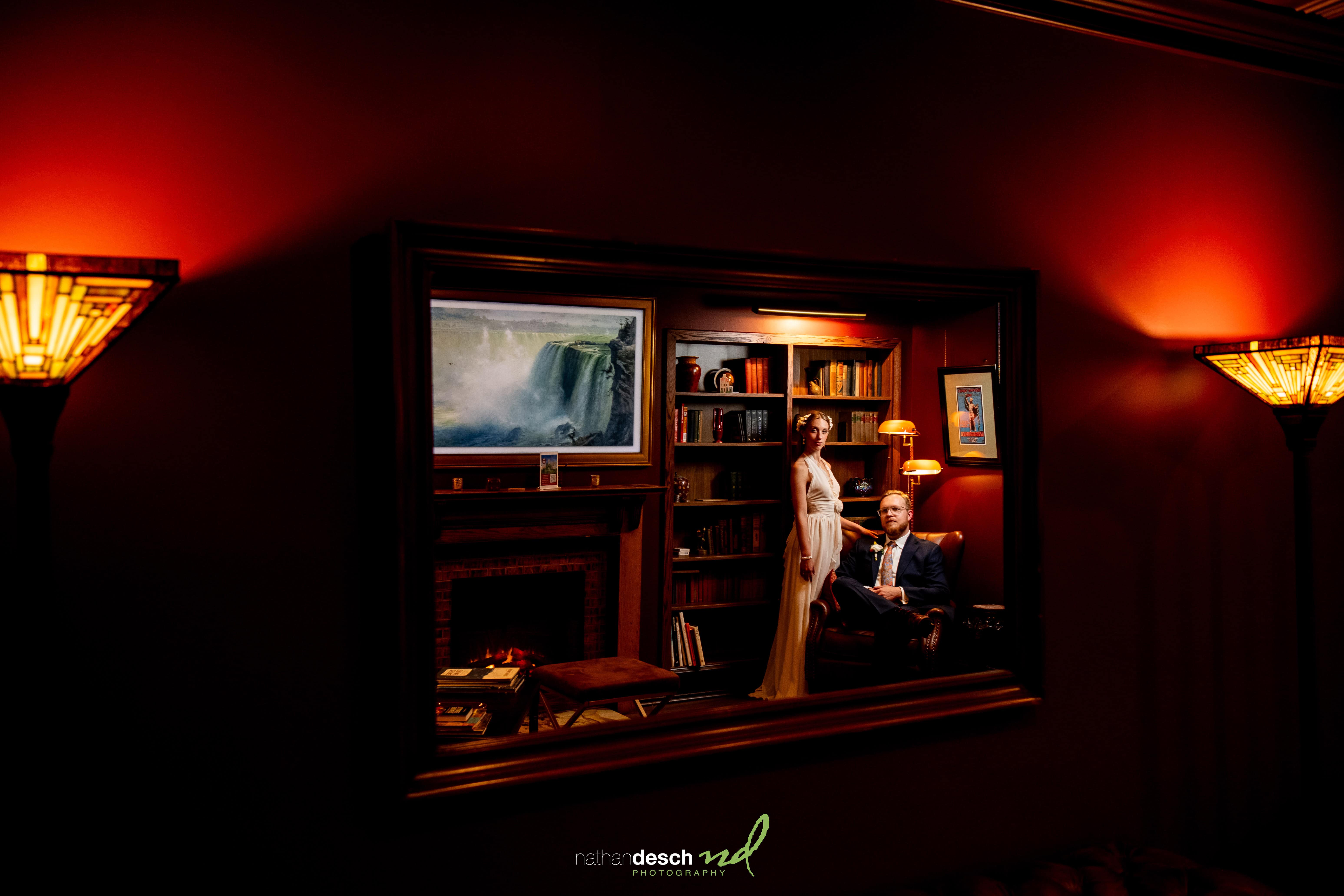 Bride and groom reflected in a large mirror in an elegant, warmly lit library at their University and Whist Club wedding.