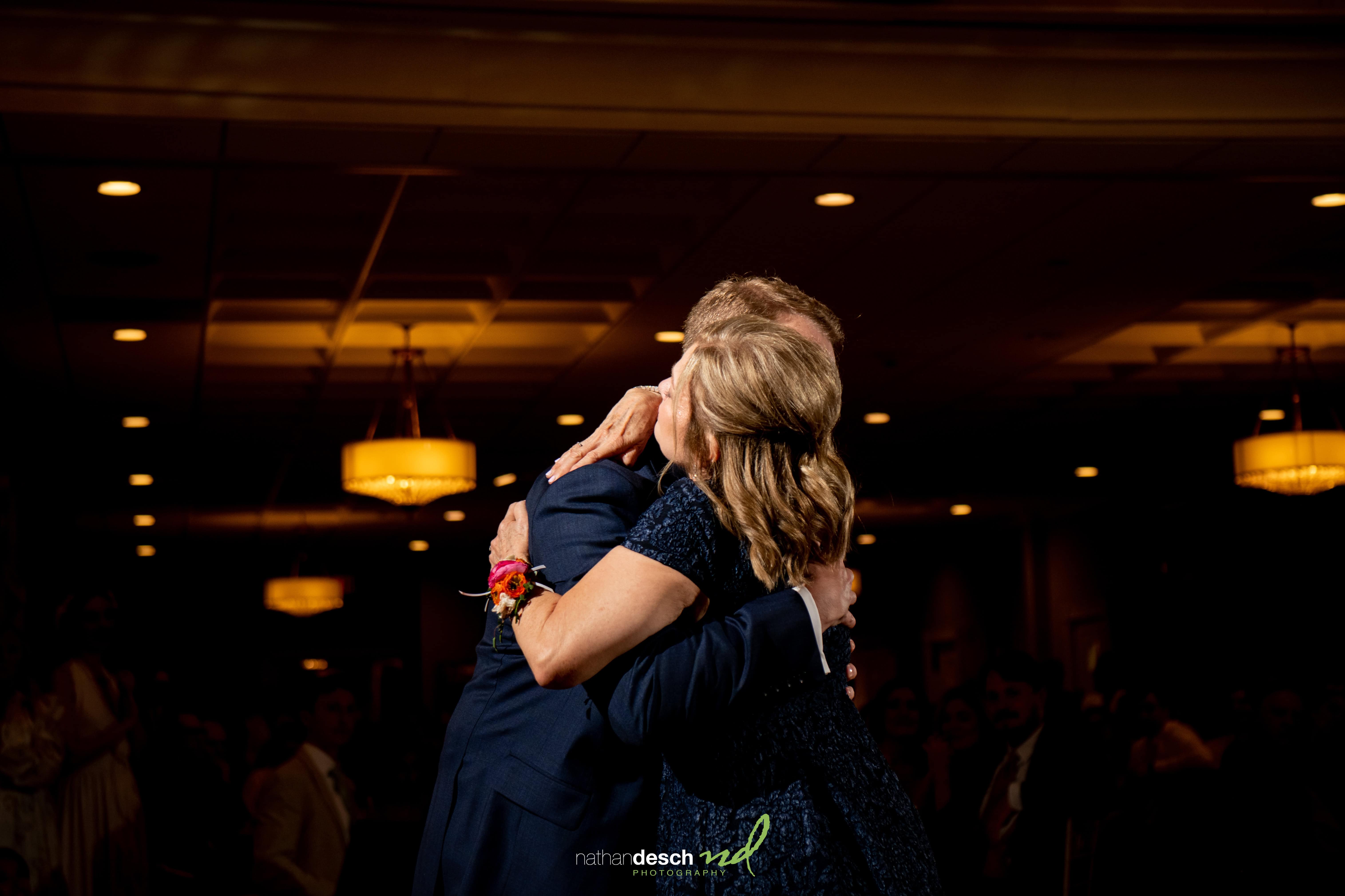 Bride in navy dress and groom in suit share a romantic dance at University and Whist Club wedding, guests look on.